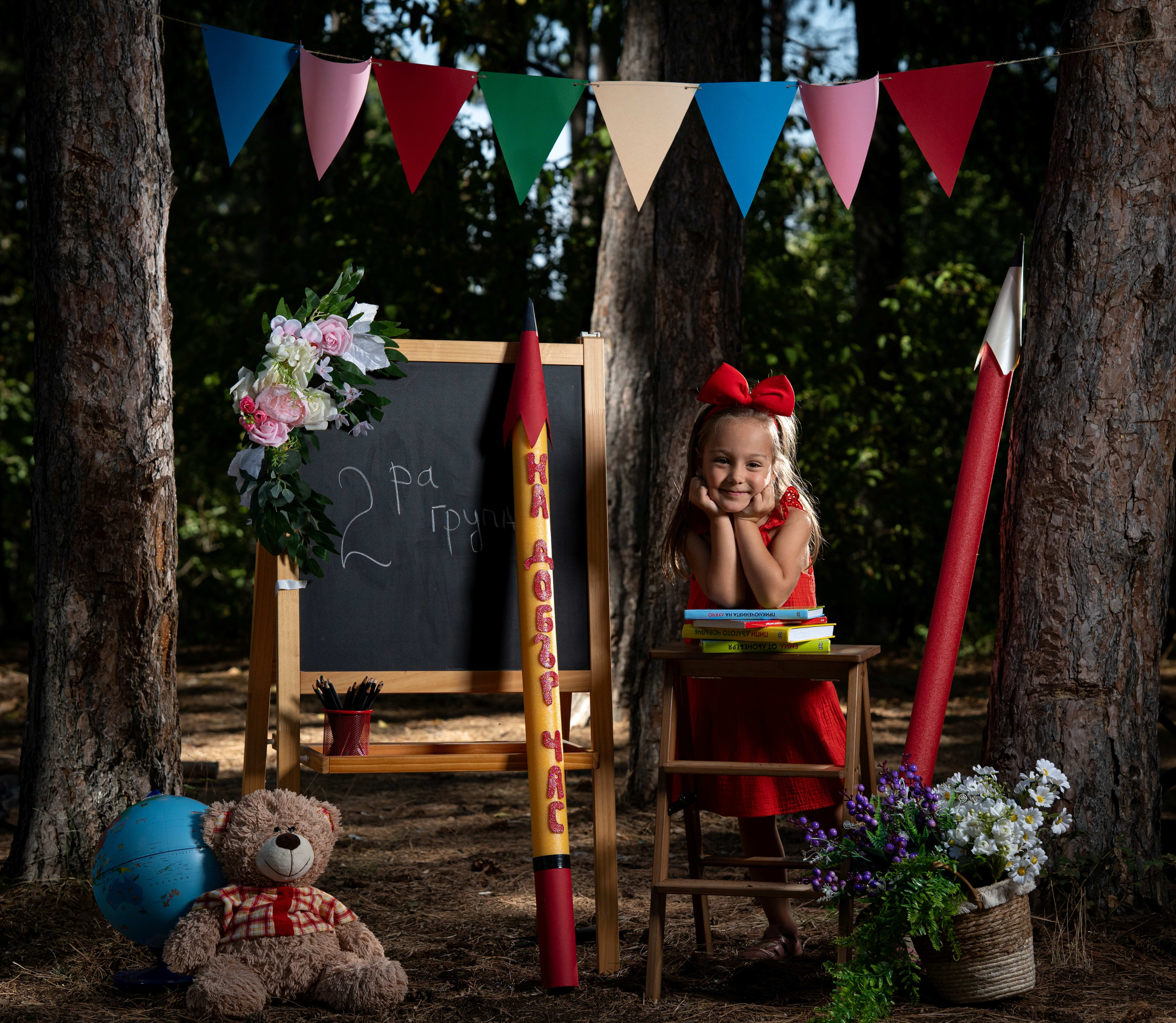 Little girl in a red dress in front of a school set with a chalkboard. On the board it says 'Group 2'.