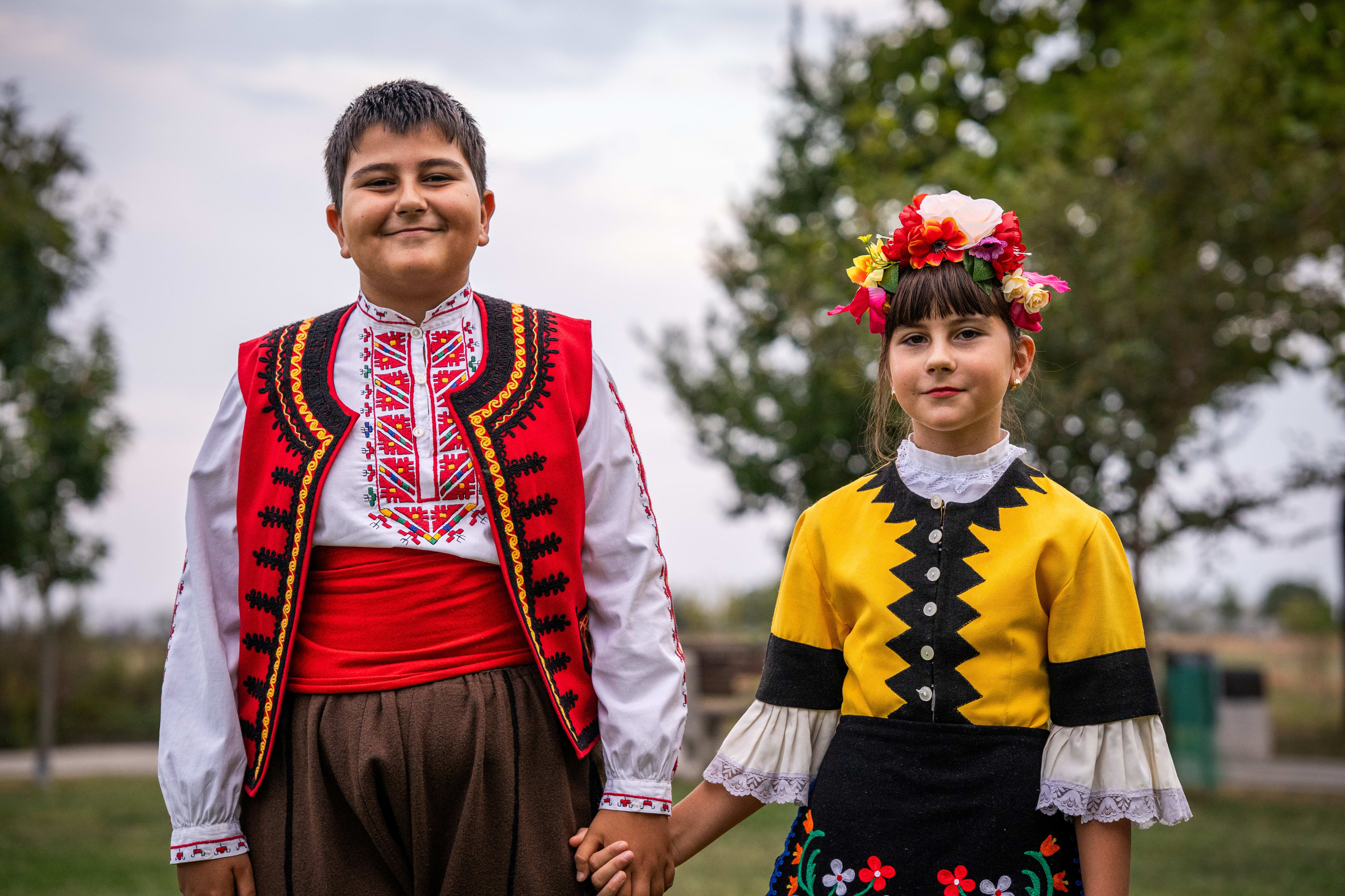 Boy and girl dressed in traditional folk costumes holding hands and smiling.