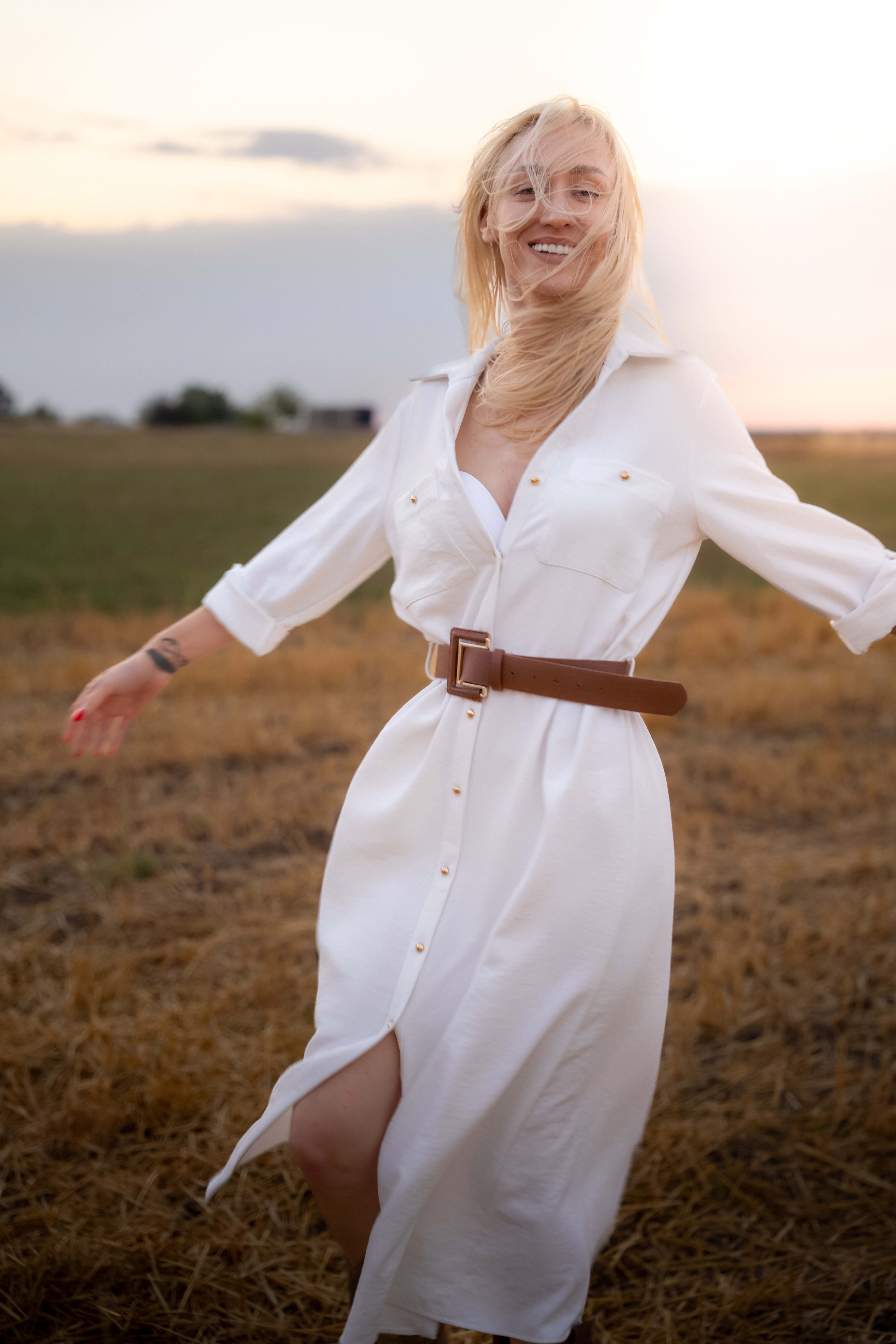 A woman dances among straw bales, dressed in a white dress. She has blonde hair and a big smile