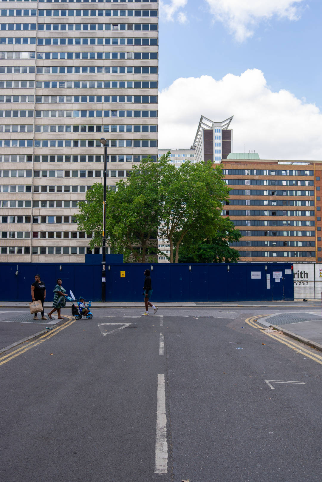 Photo of a blue constructions hoarding around an empty building site, with a tree visible on the distance