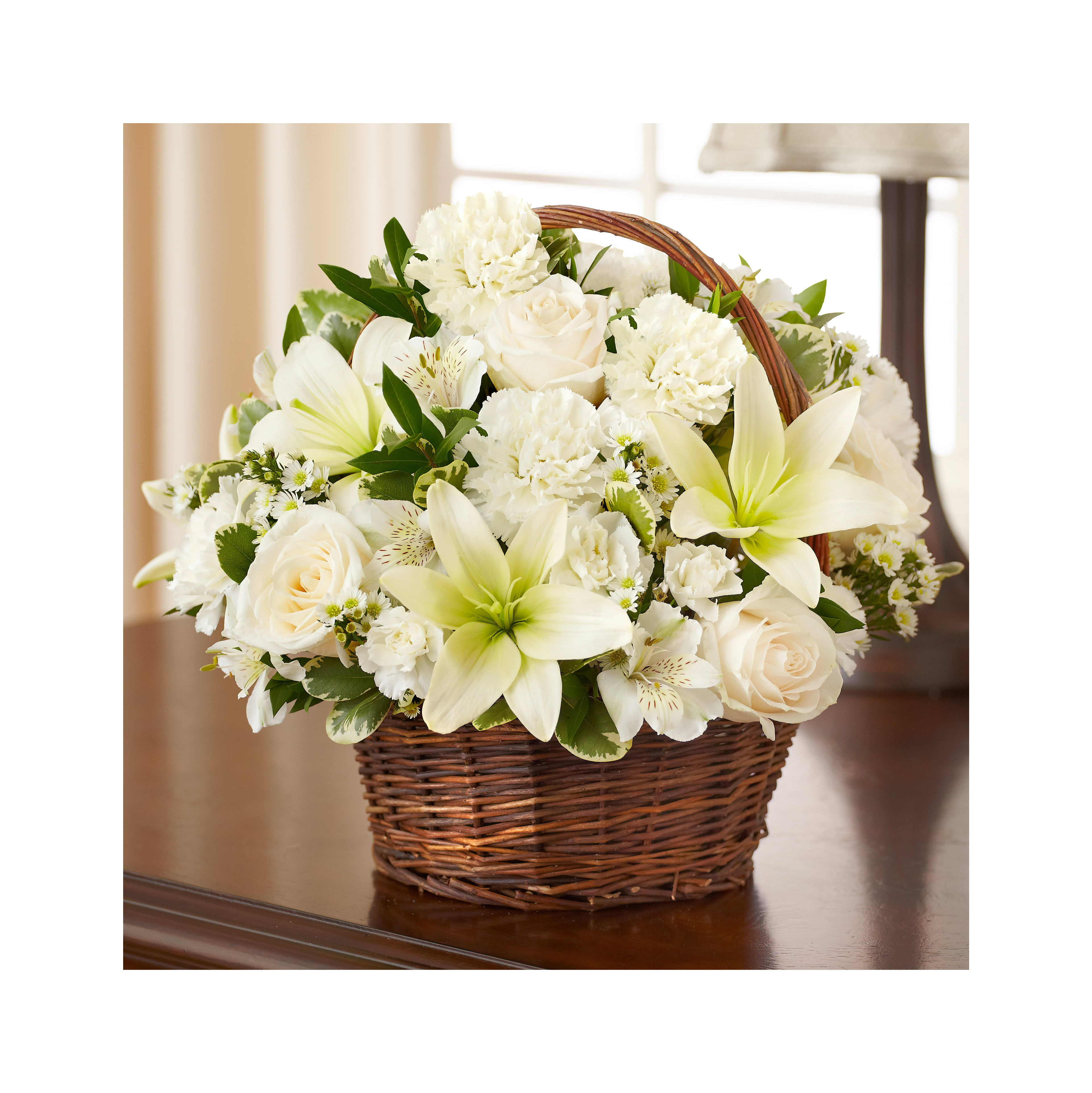 A beautiful wicker basket holds an assortment of white flowers including lilies and roses.