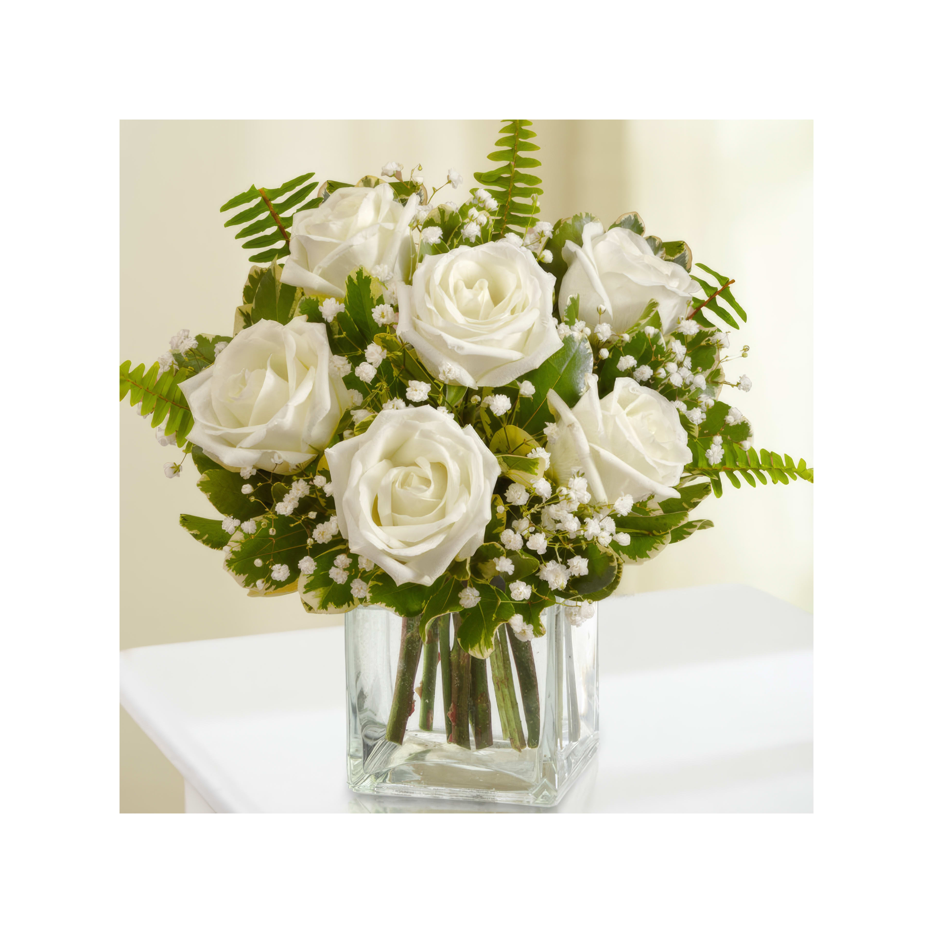 A beautiful arrangement of white roses with ferns in a clear glass vase is displayed indoors.