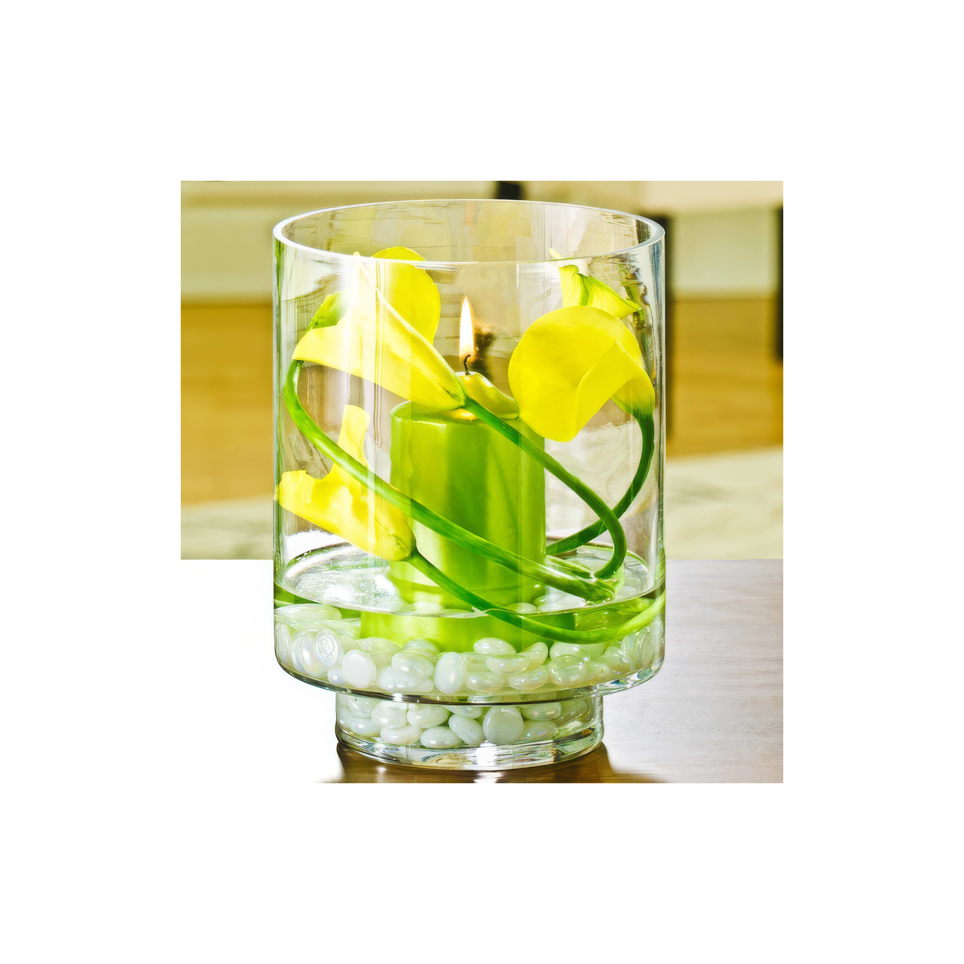 A vibrant glass vase holds yellow flowers, a green candle, and white pebbles, enhancing the decor.