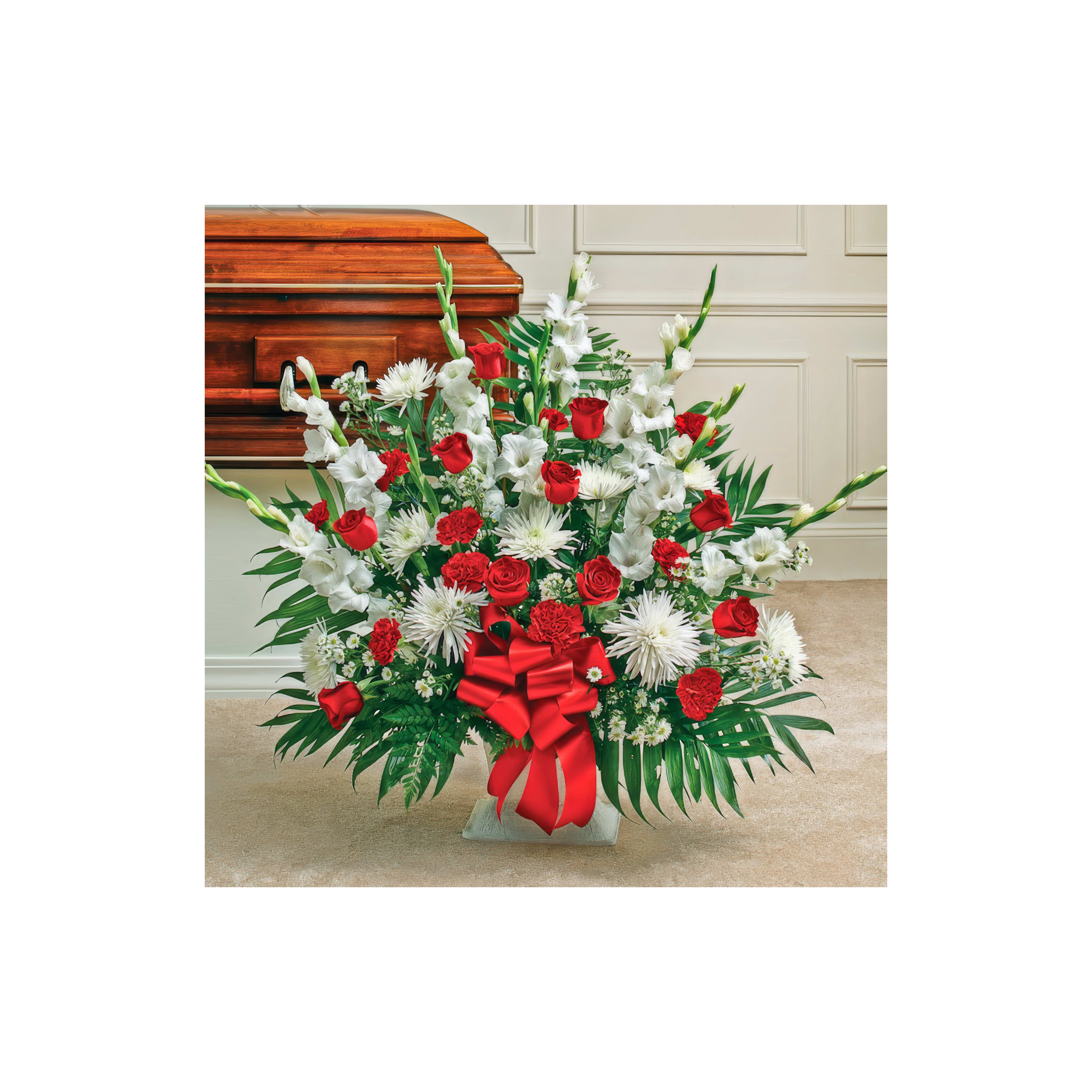 A touching floral tribute of red roses and white flowers next to a wooden casket.