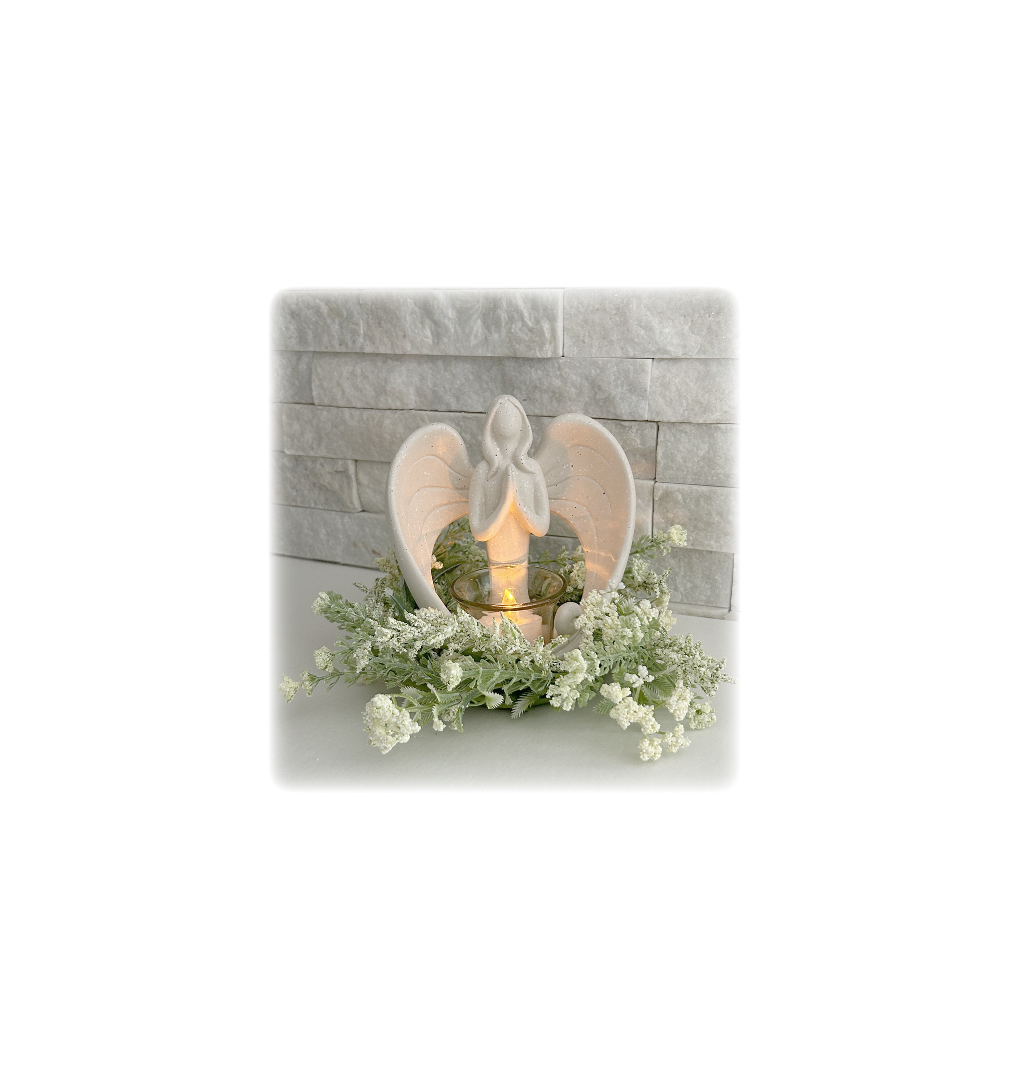 An angel candle holder surrounded by dried flowers on a shelf by a stone wall.