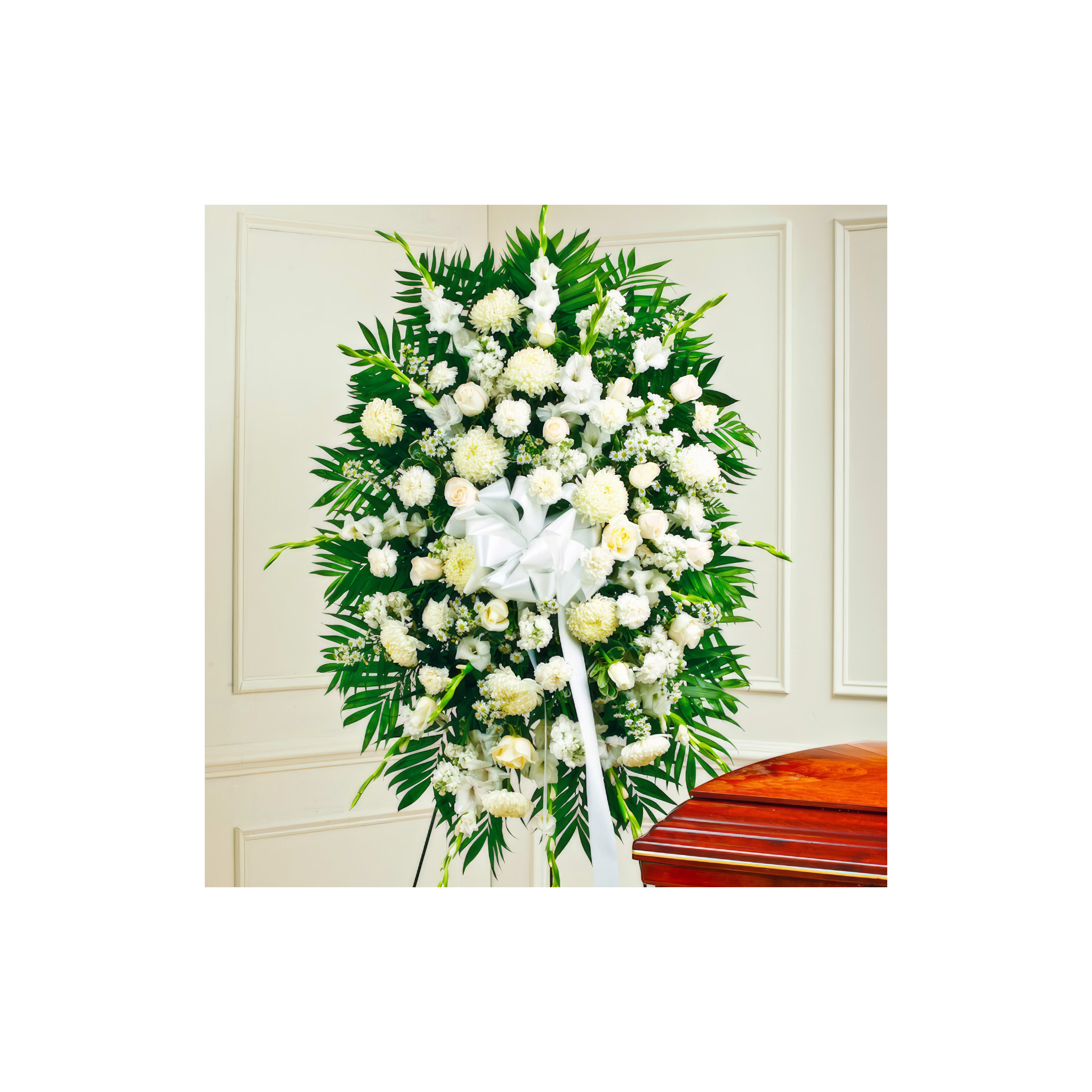 White flowers and greenery are arranged beautifully near a wooden coffin at a memorial service.