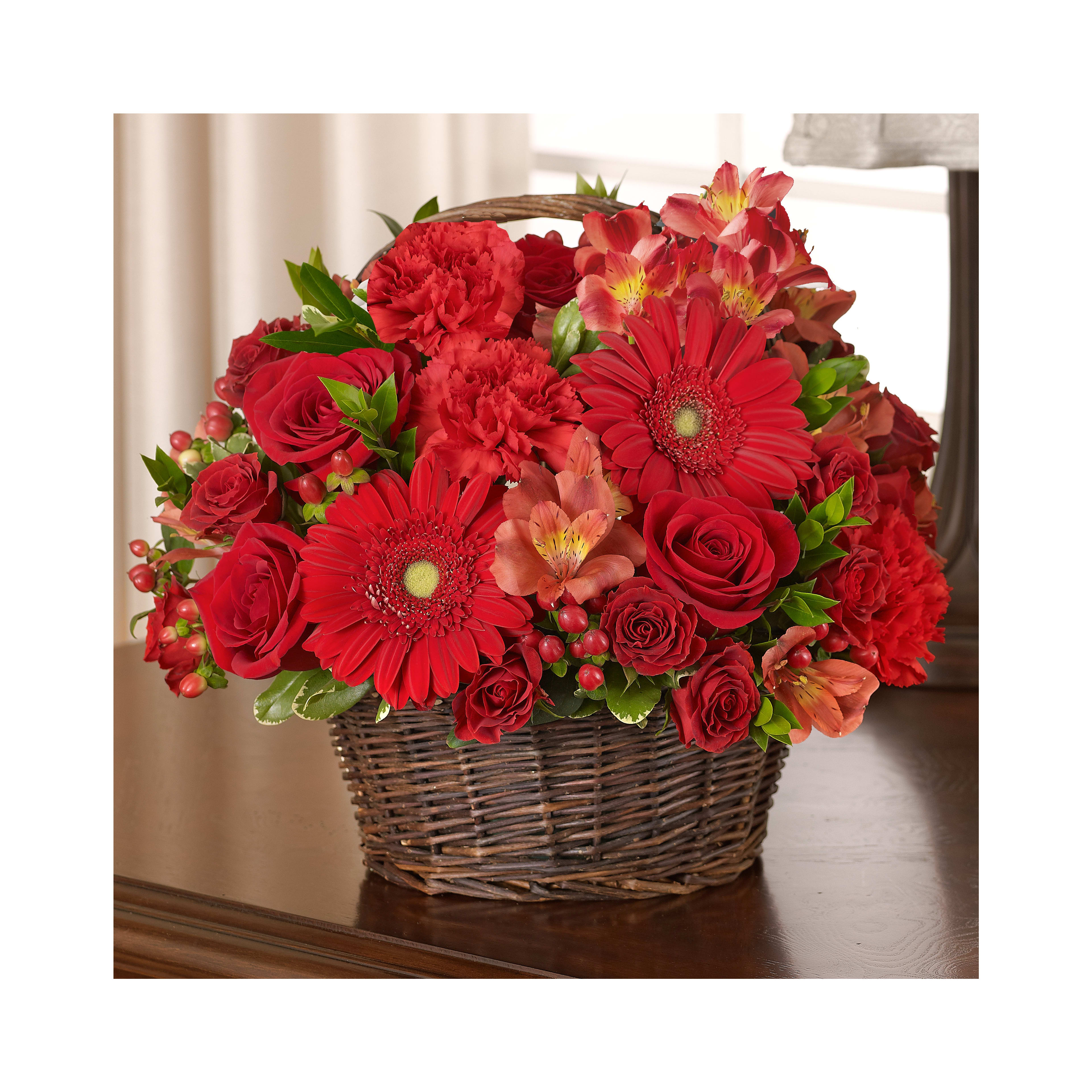 A vibrant arrangement of red flowers in a decorative basket placed on a wooden table.