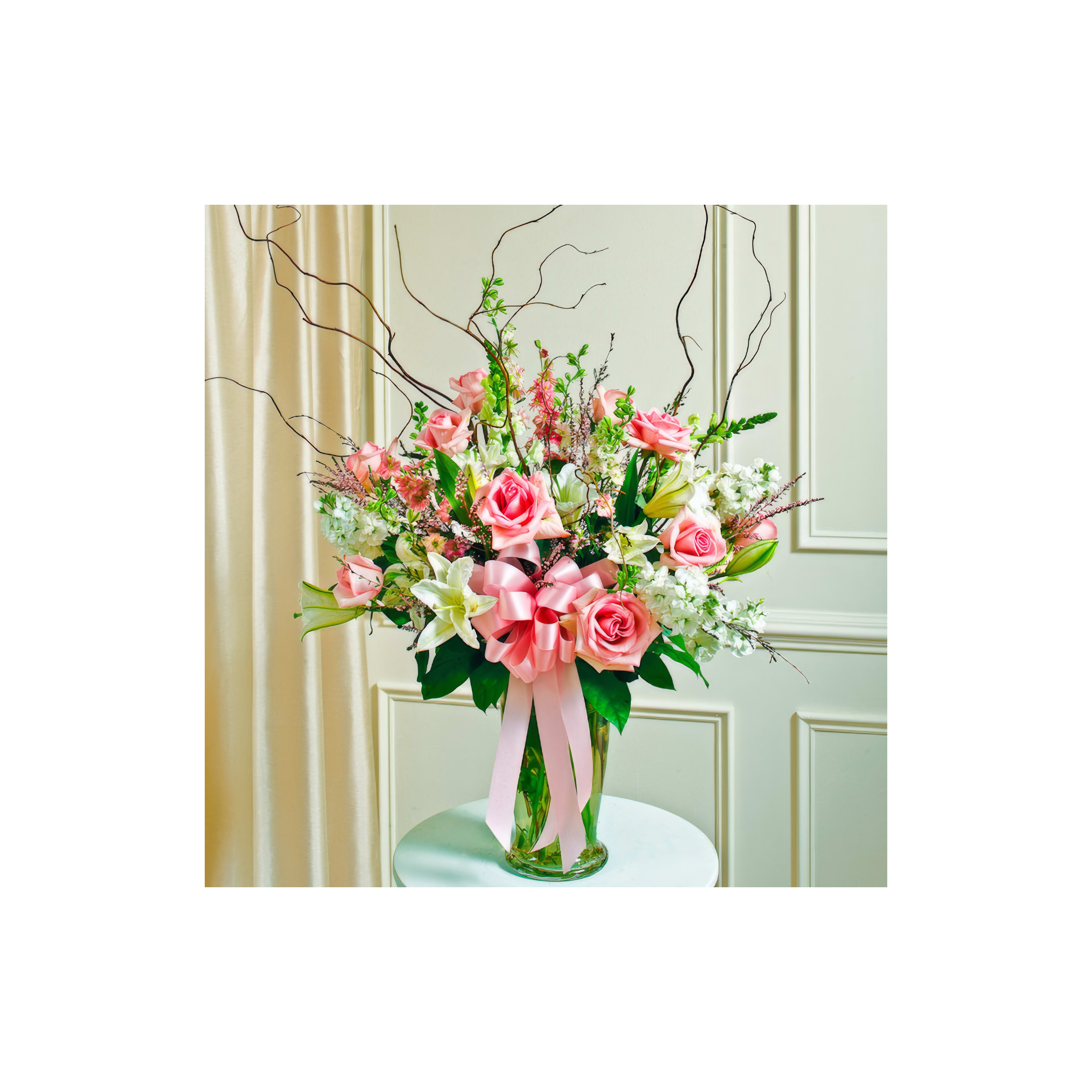 Colorful bouquet includes pink roses, white lilies, and greenery in a stylish glass vase.