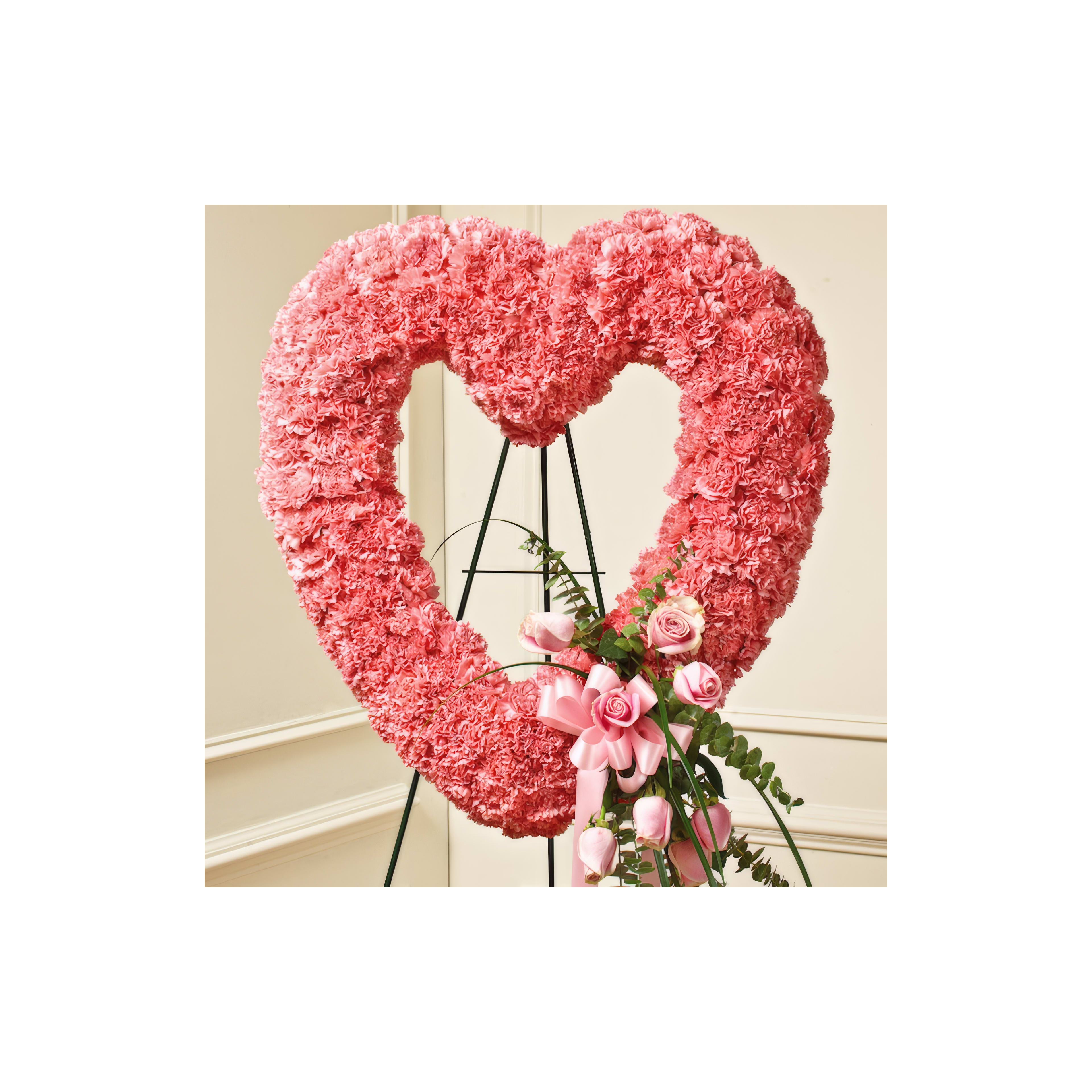 A vibrant heart-shaped floral arrangement rests on an elegant stand, adorned with pink roses.