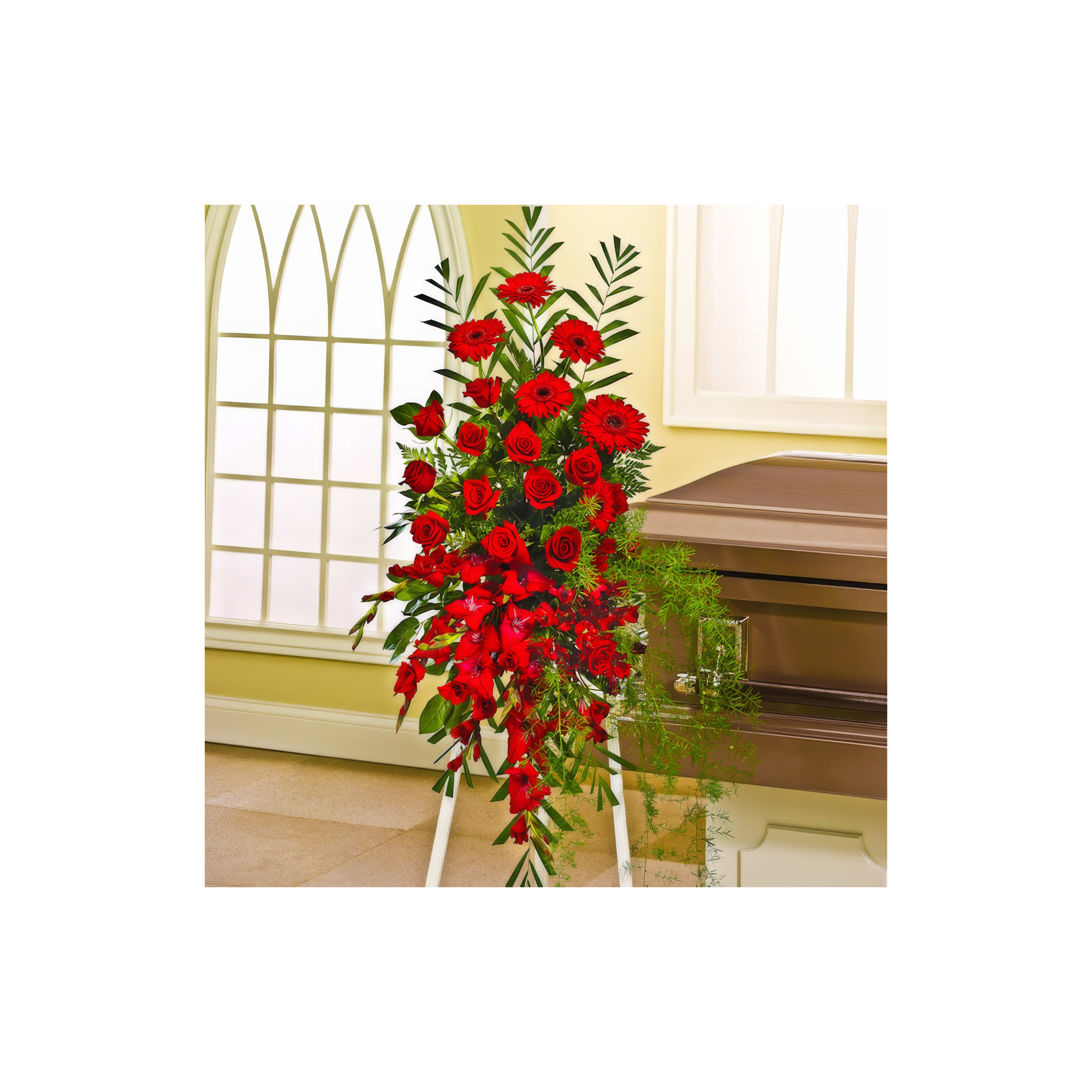 Bright red flowers, including roses and lilies, stand beside a casket in a calm, indoor space.