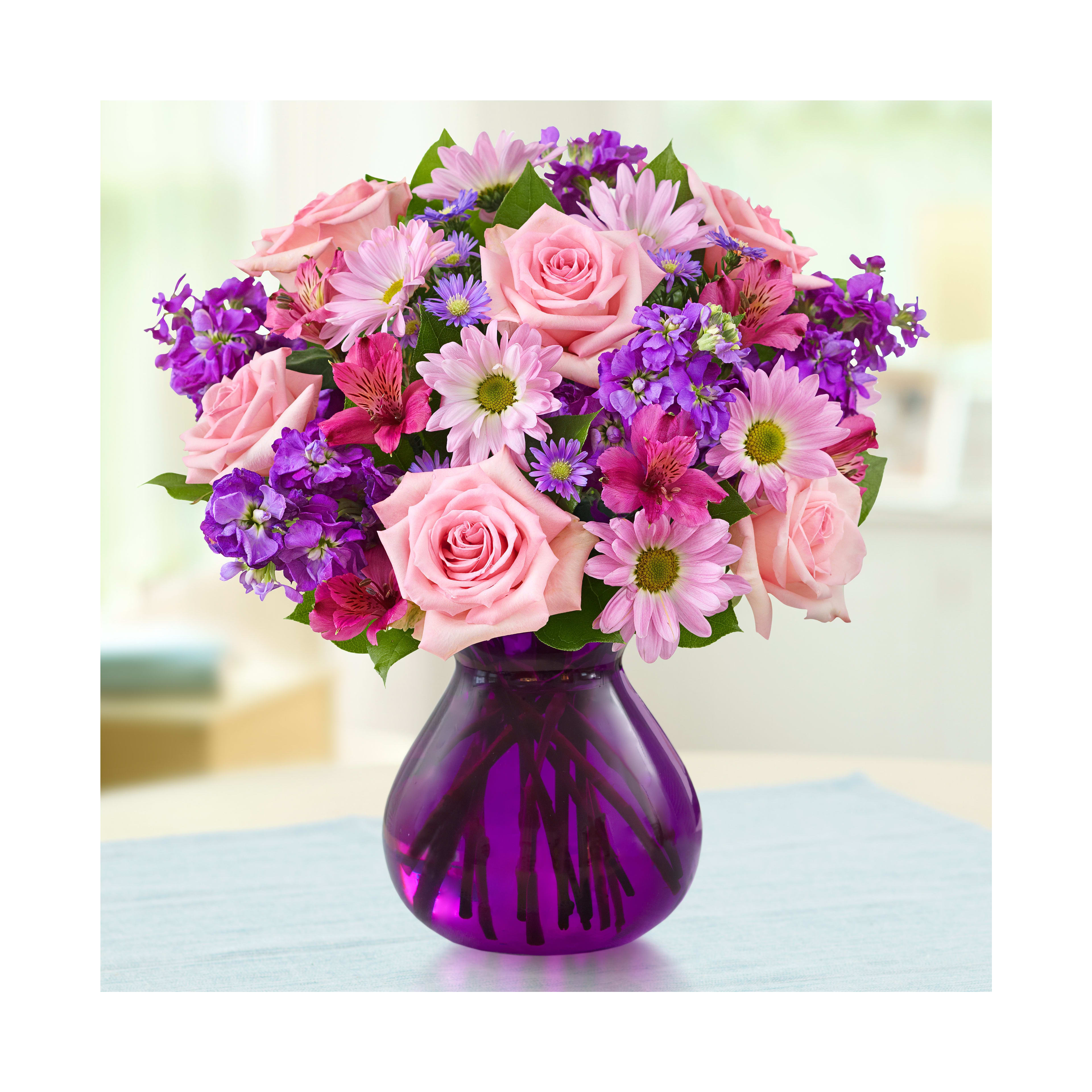 Bright bouquet of pink roses and purple daisies displays vibrant colors on a table indoors.