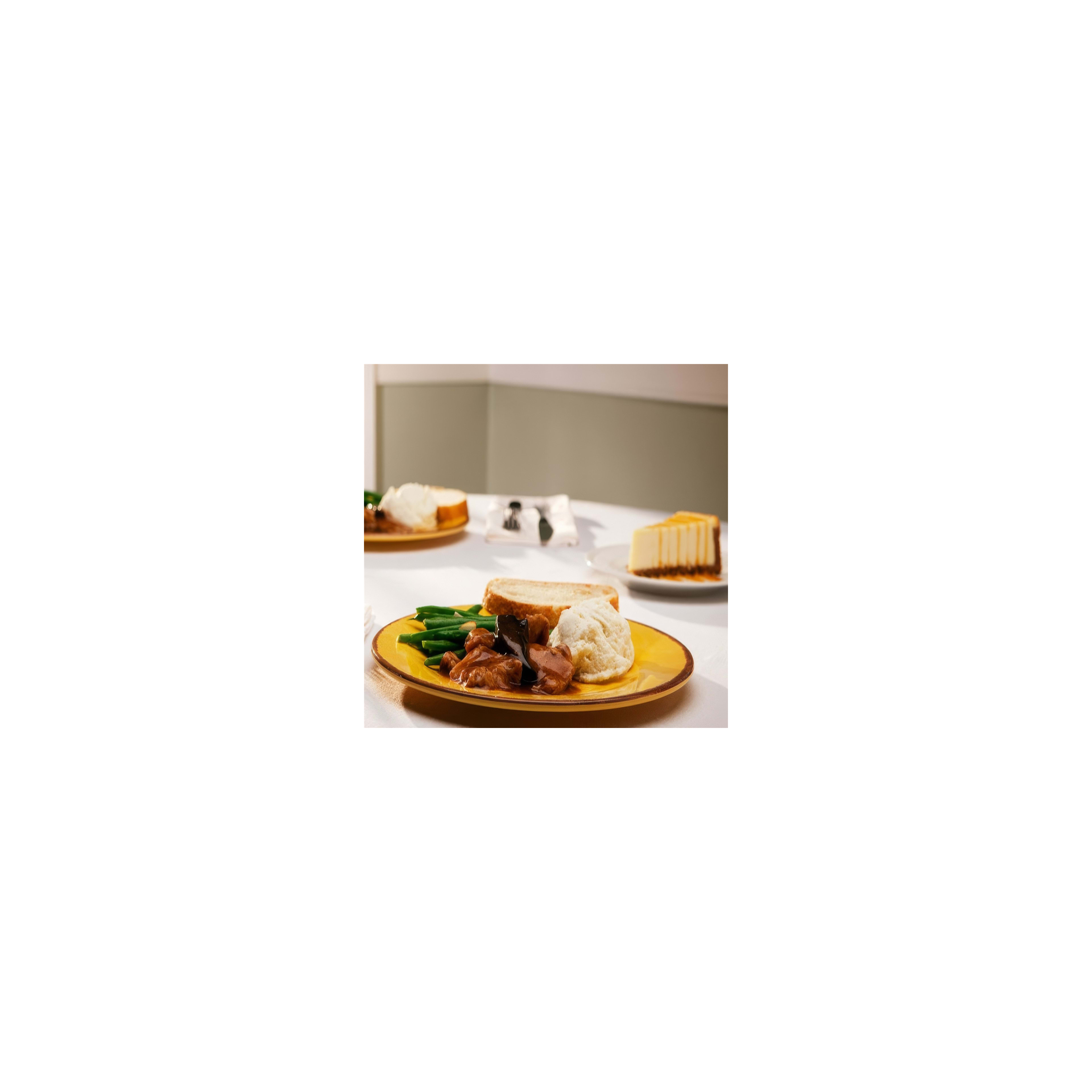 A tasty home-cooked meal with green beans, meat, bread, and cheesecake on a table setting.