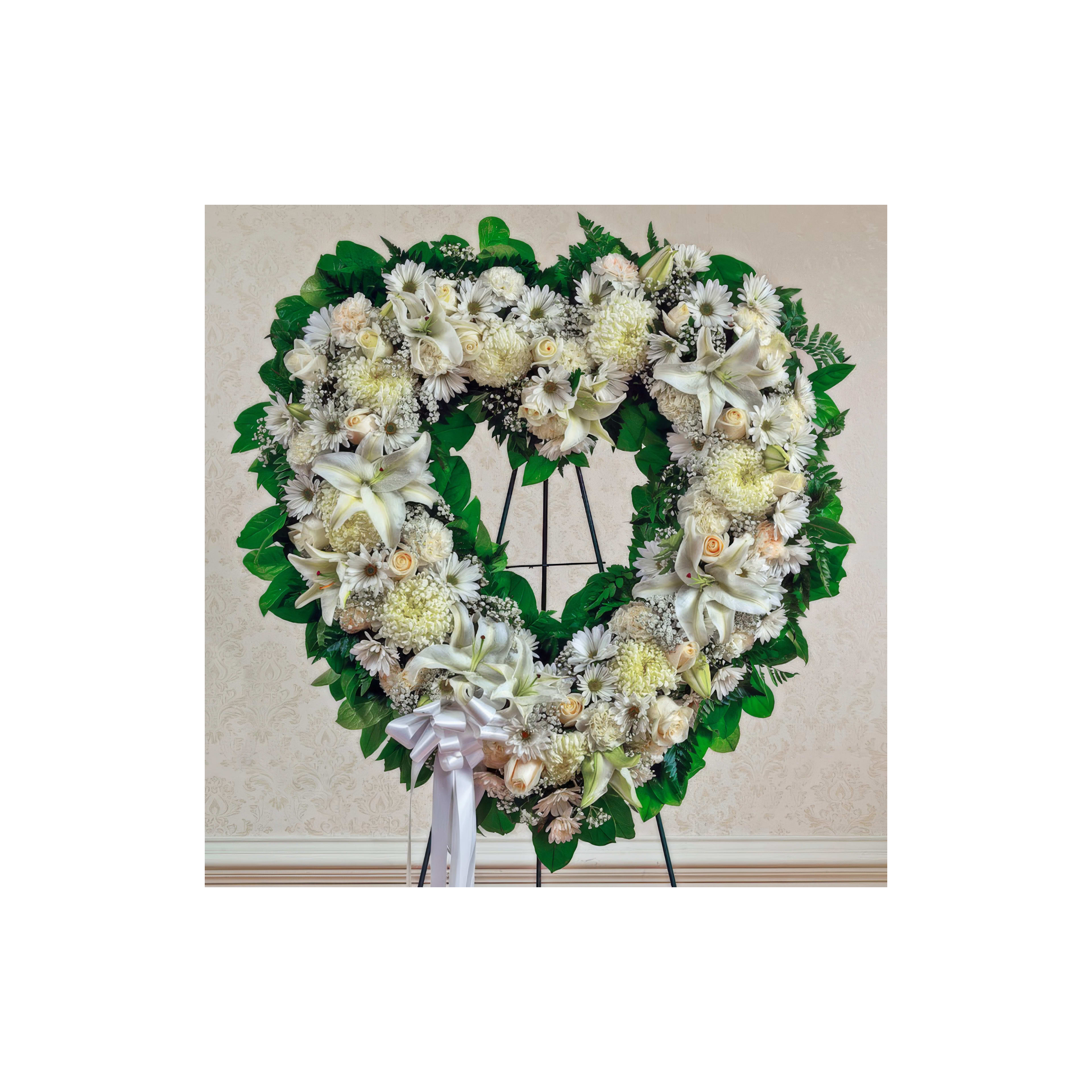 A heart-shaped floral tribute of white flowers and greenery stands on a display.