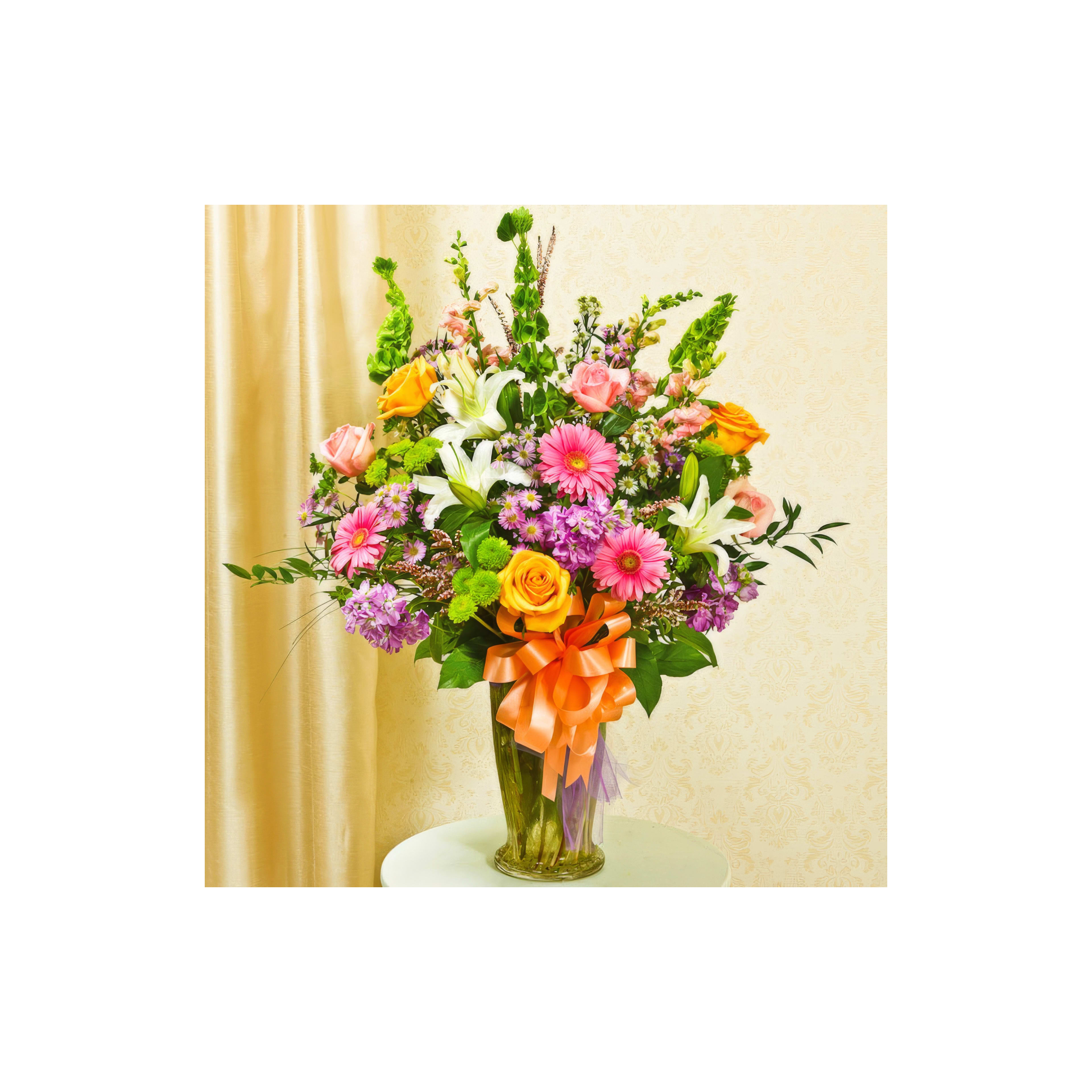 Colorful bouquet features pink gerbera daisies, orange roses, and purple flowers in a vase.