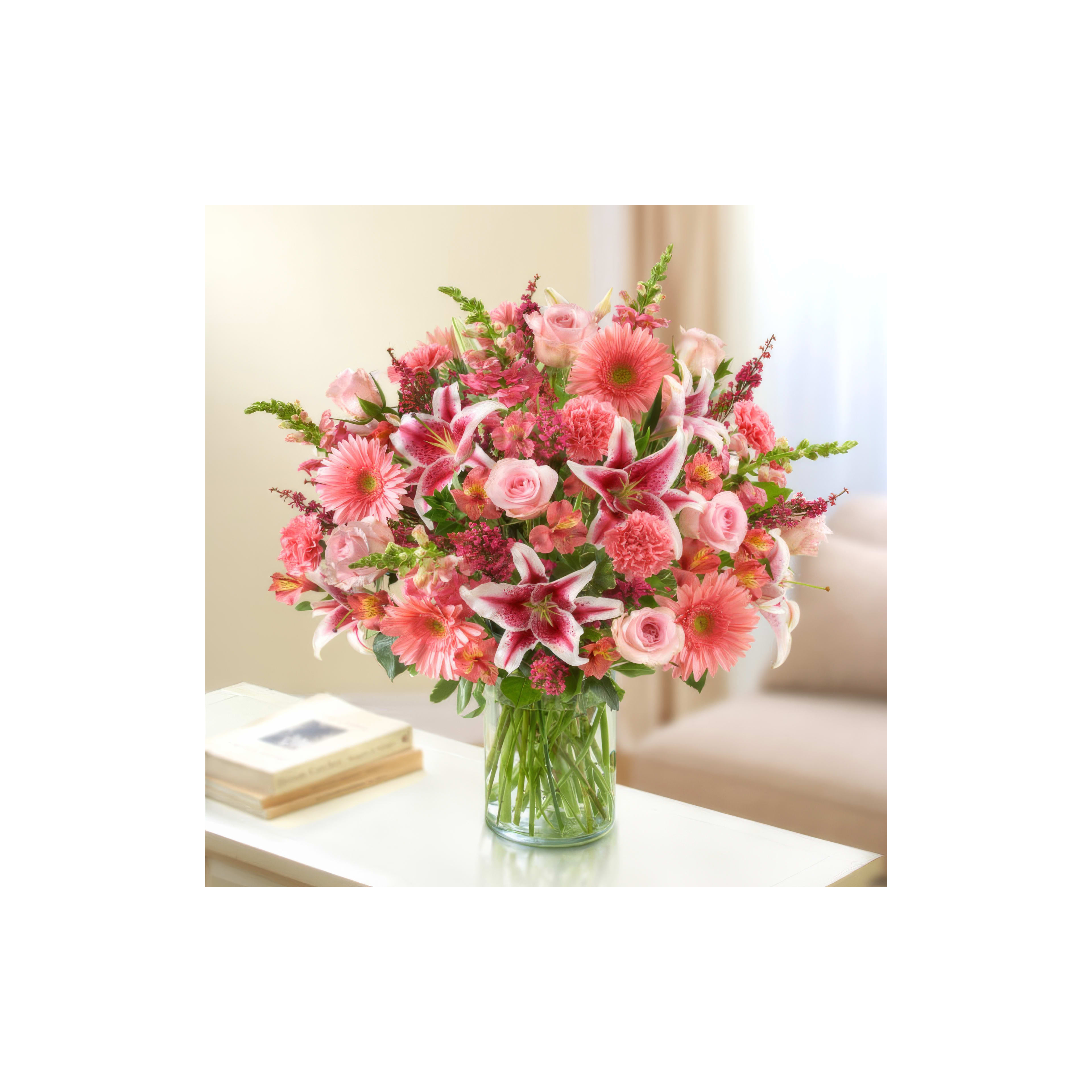 A beautifully arranged bouquet of pink flowers stands in a vase on a table in a light-filled room.