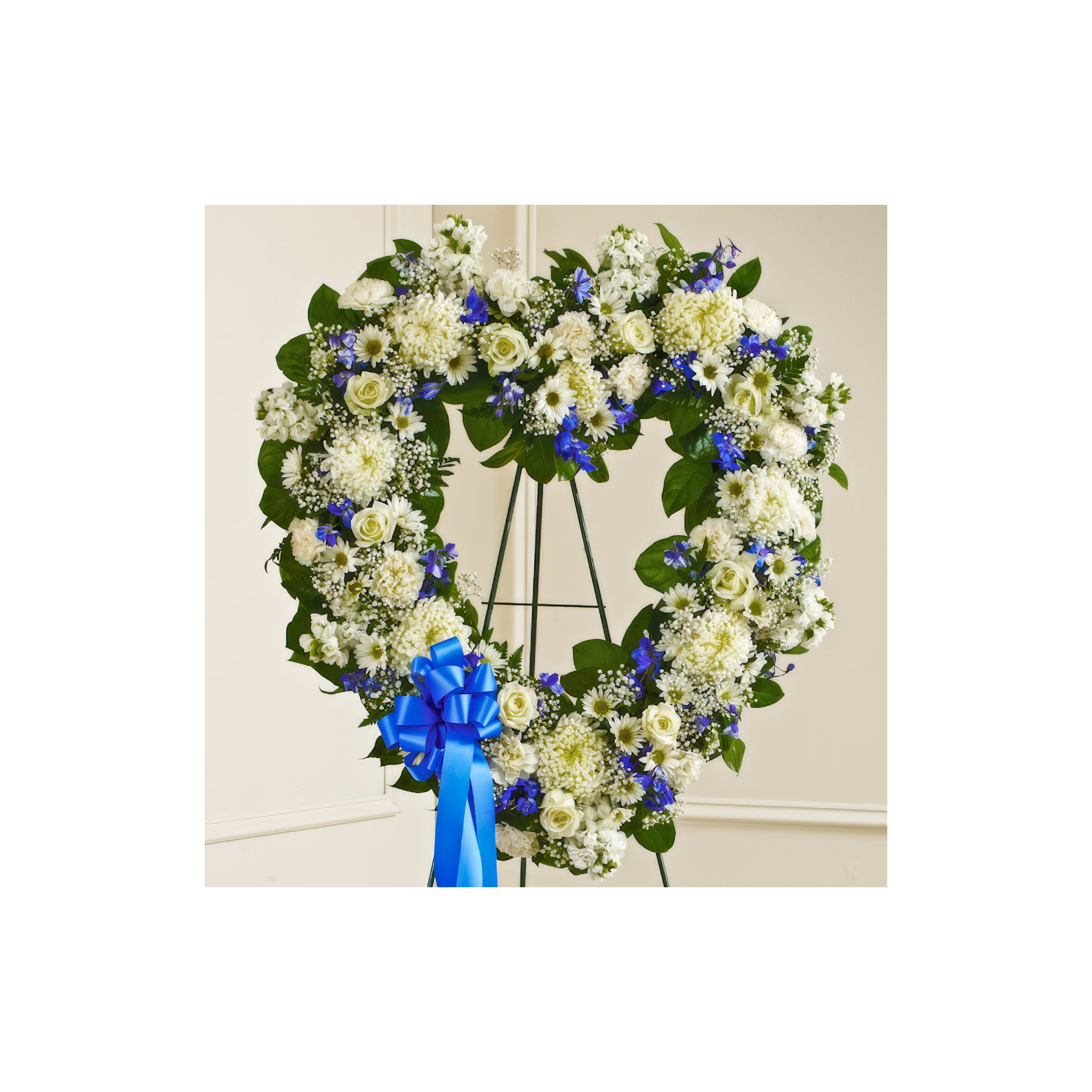 A heart-shaped floral arrangement is displayed on an easel, featuring white and blue flowers.