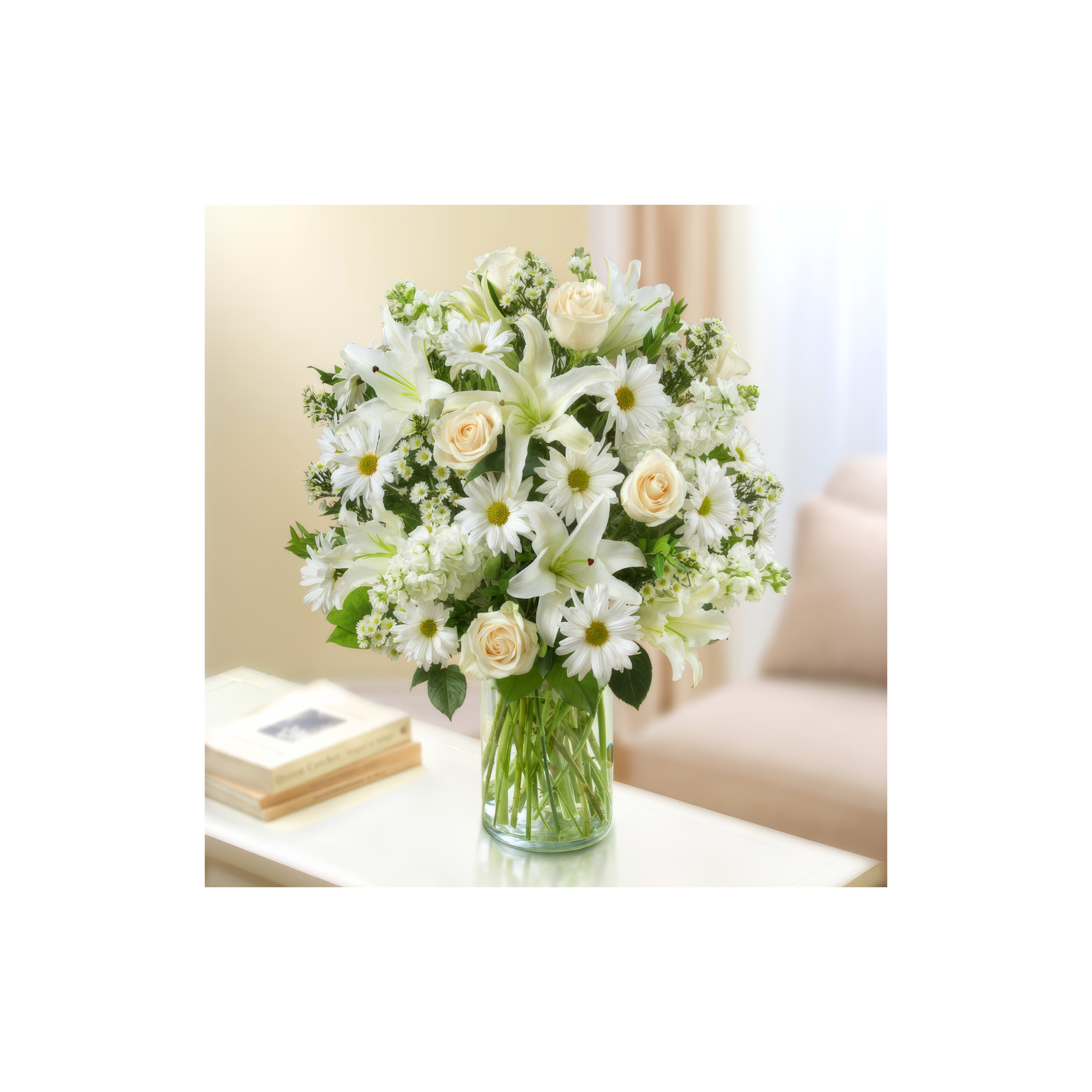 A vibrant arrangement of white lilies, daisies, and roses sits elegantly in a clear vase on a table.