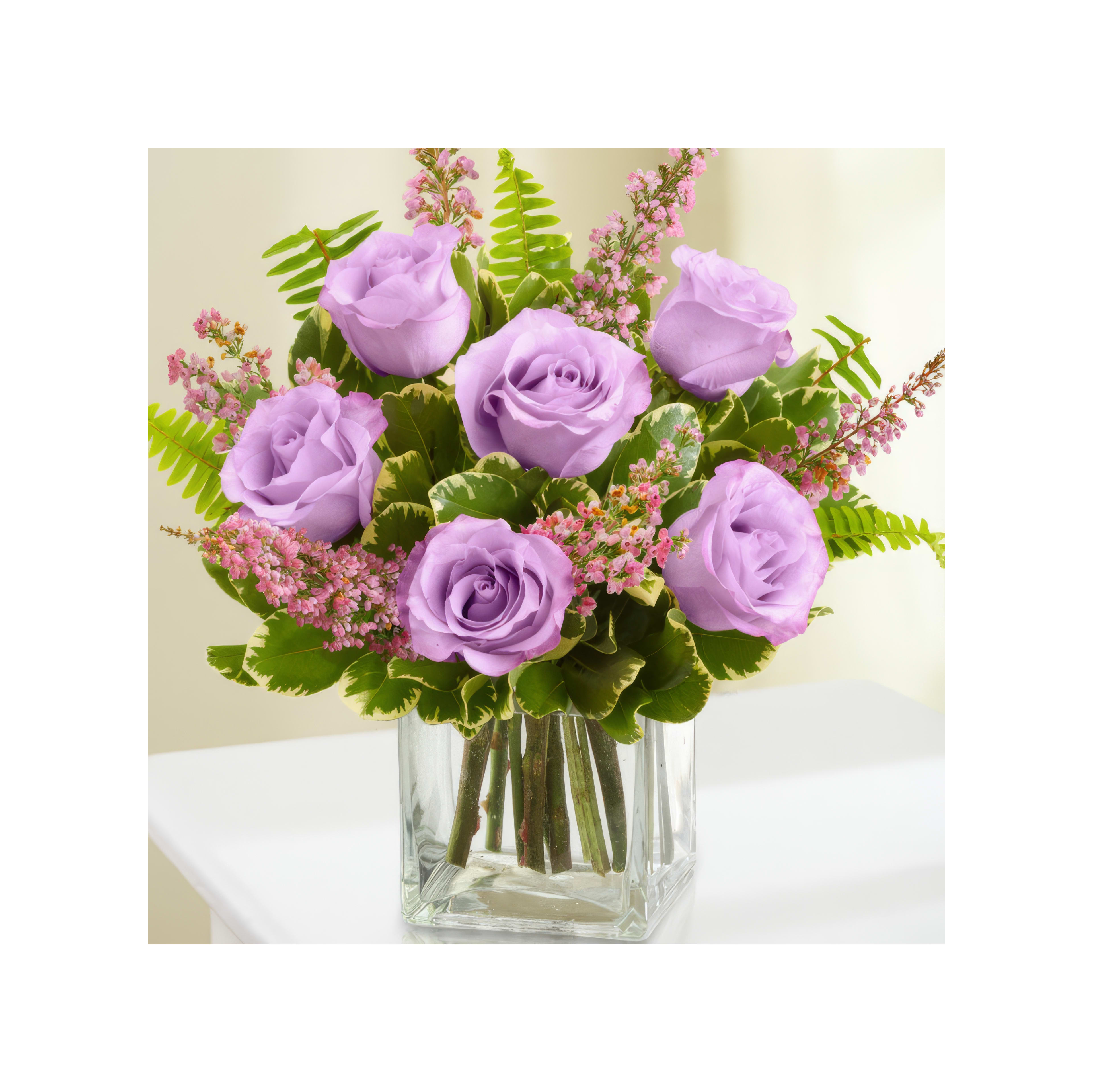 A bouquet of lavender roses in a glass vase, accented by greenery and pink blooms.