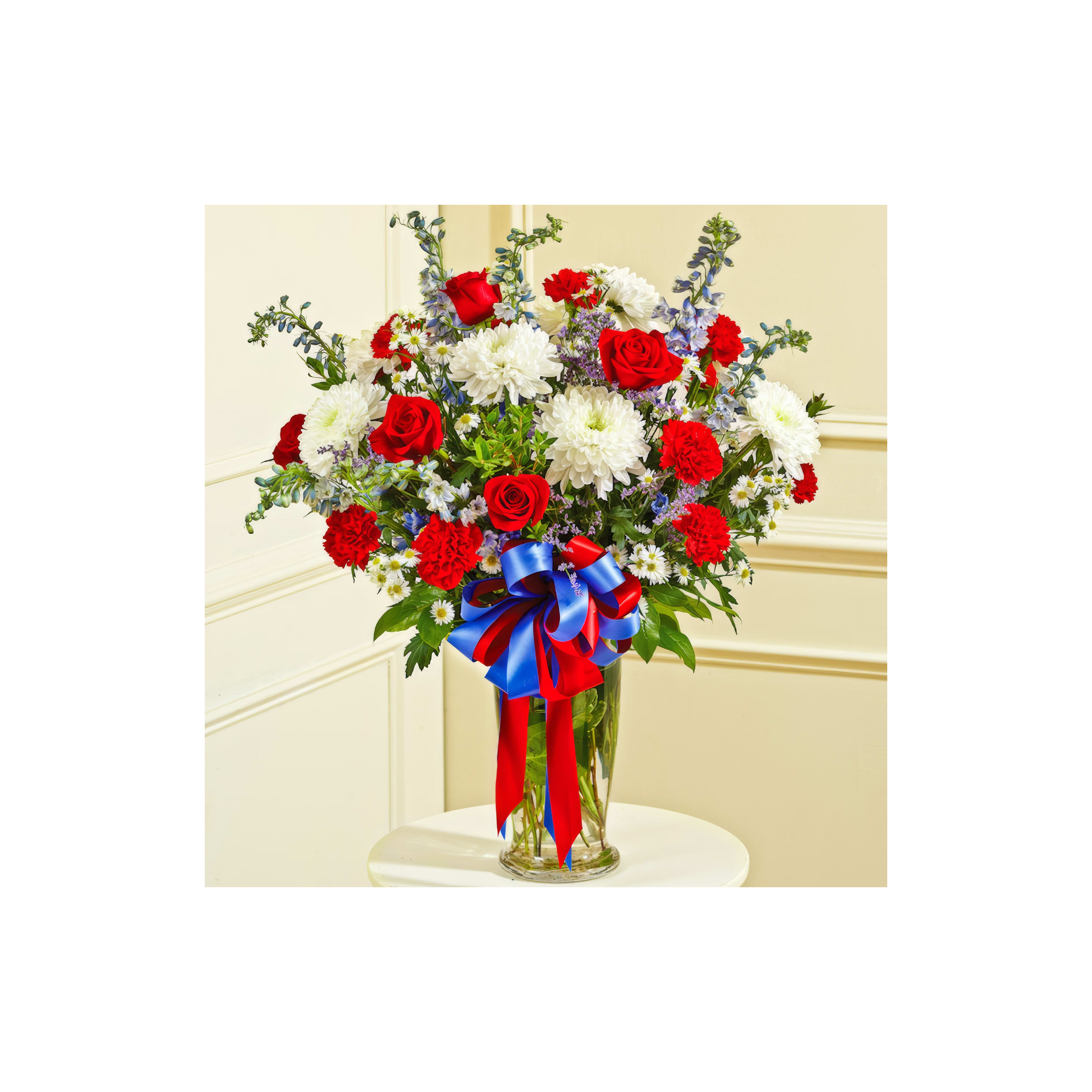 Bright bouquet featuring red roses, white chrysanthemums, and blue flowers in a decorative vase.