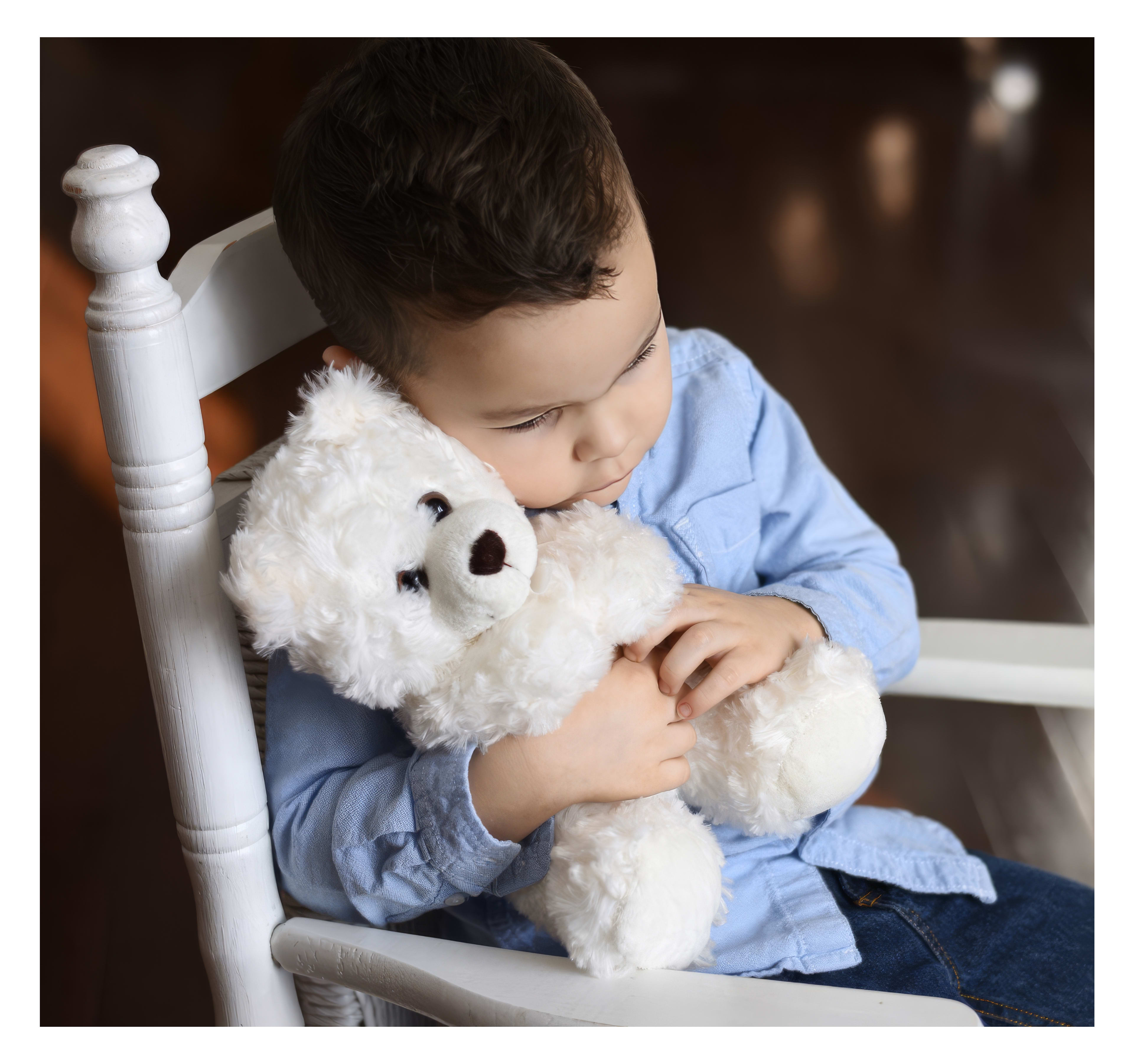 A small child embraces a fluffy white teddy bear while relaxing in a chair, showcasing tenderness.
