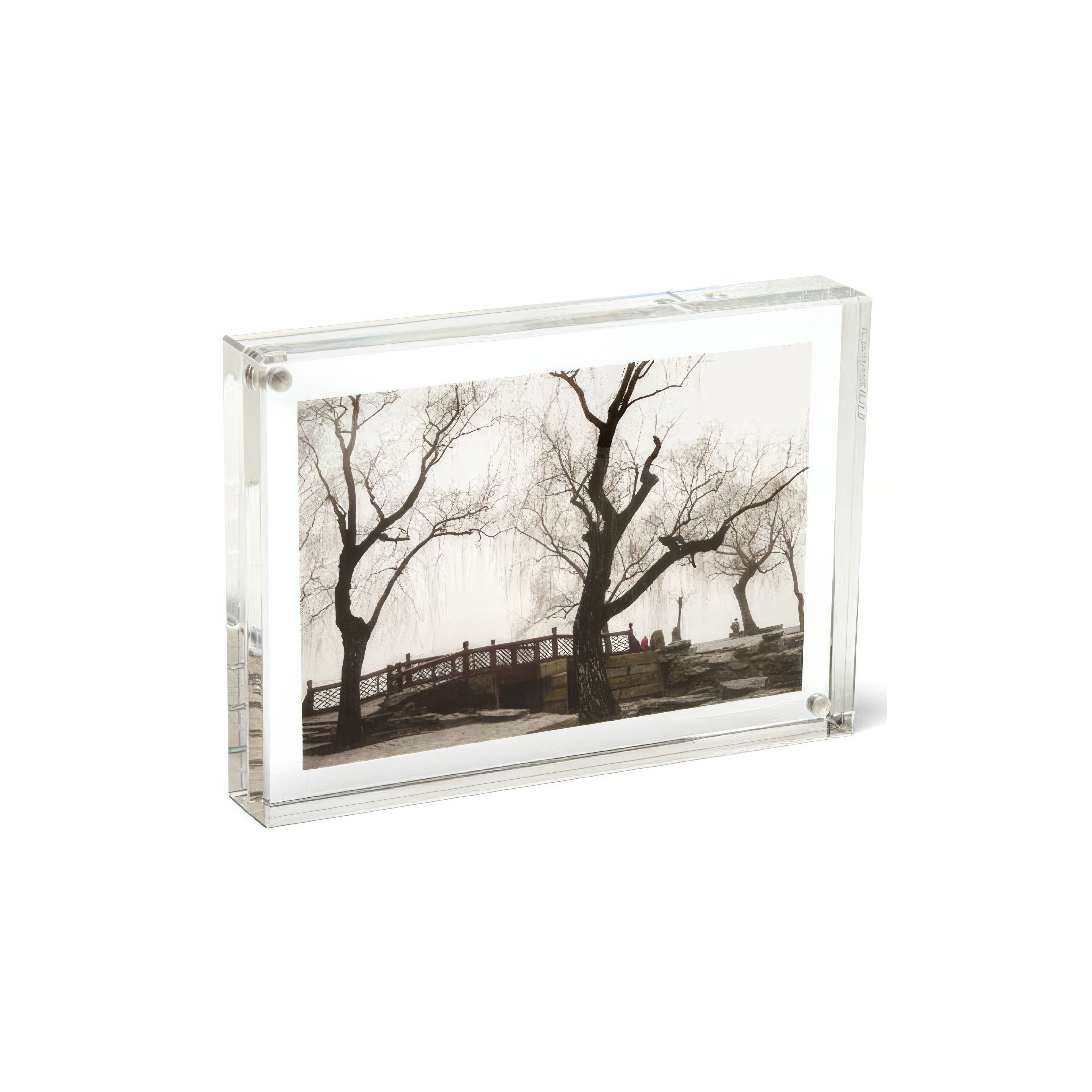 Silhouettes of bare trees and a small bridge create a serene winter landscape at dusk.
