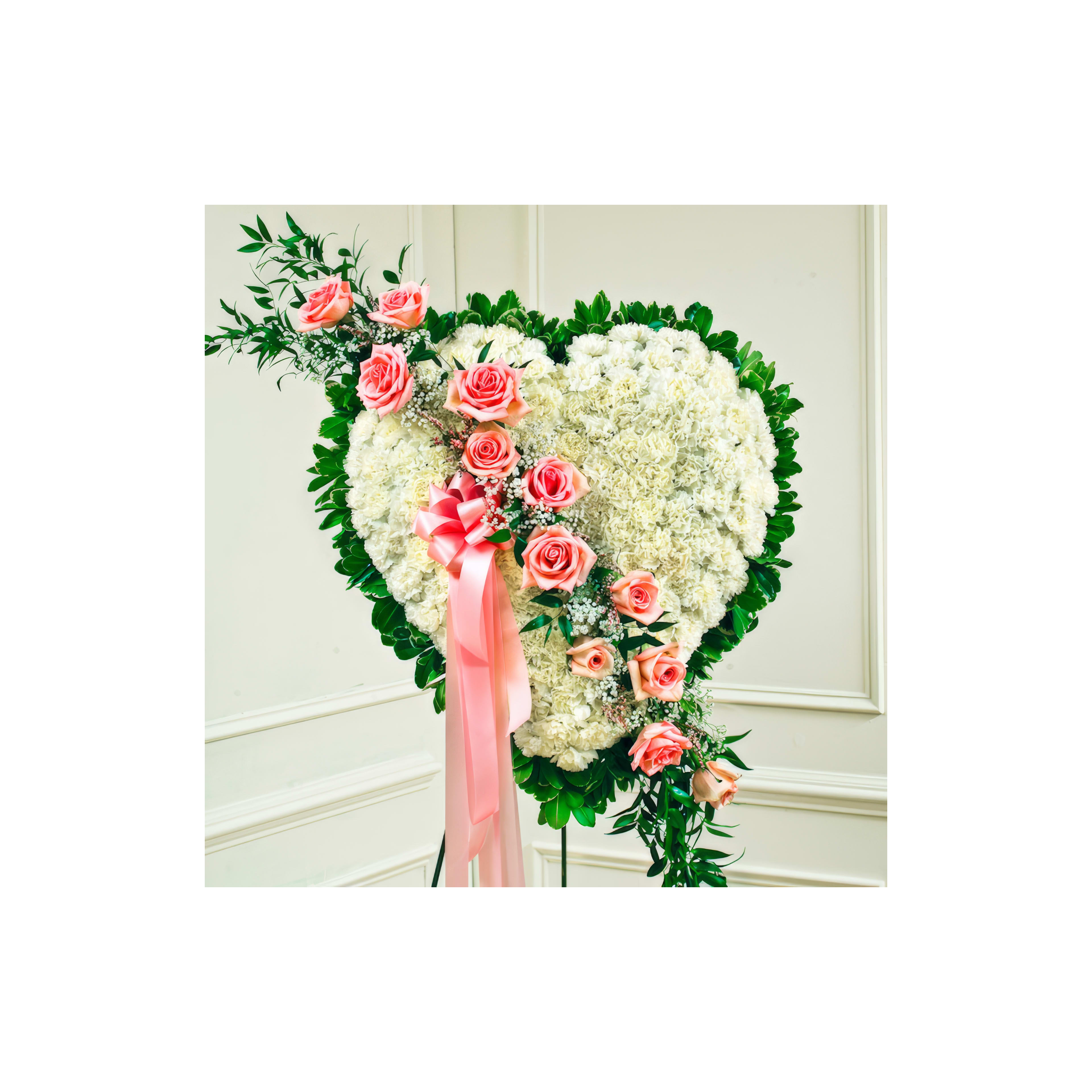 A heart-shaped floral display of white flowers and pink roses, accented with greenery.