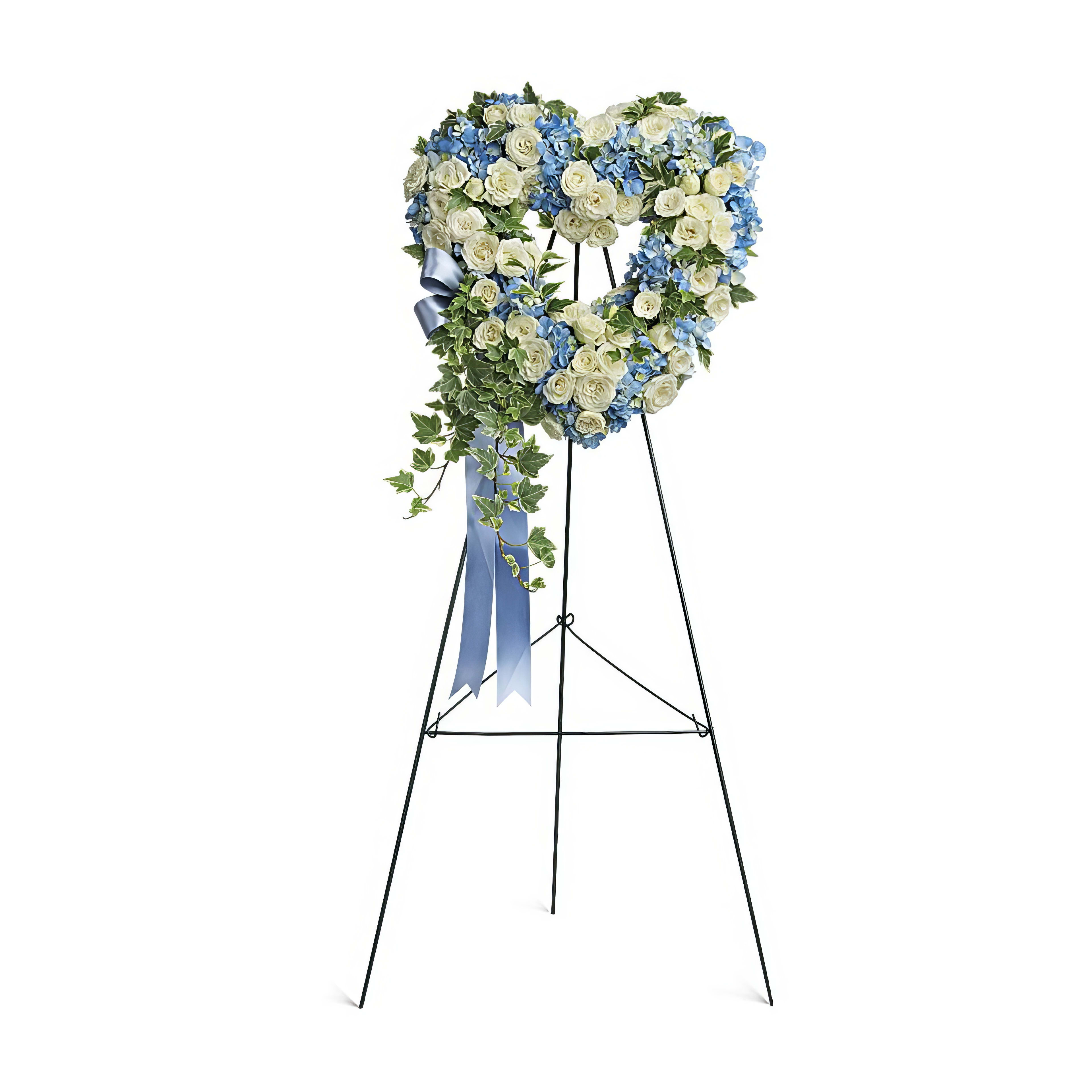 Heart-shaped arrangement with blue and white flowers placed on a tripod stand for remembrance.