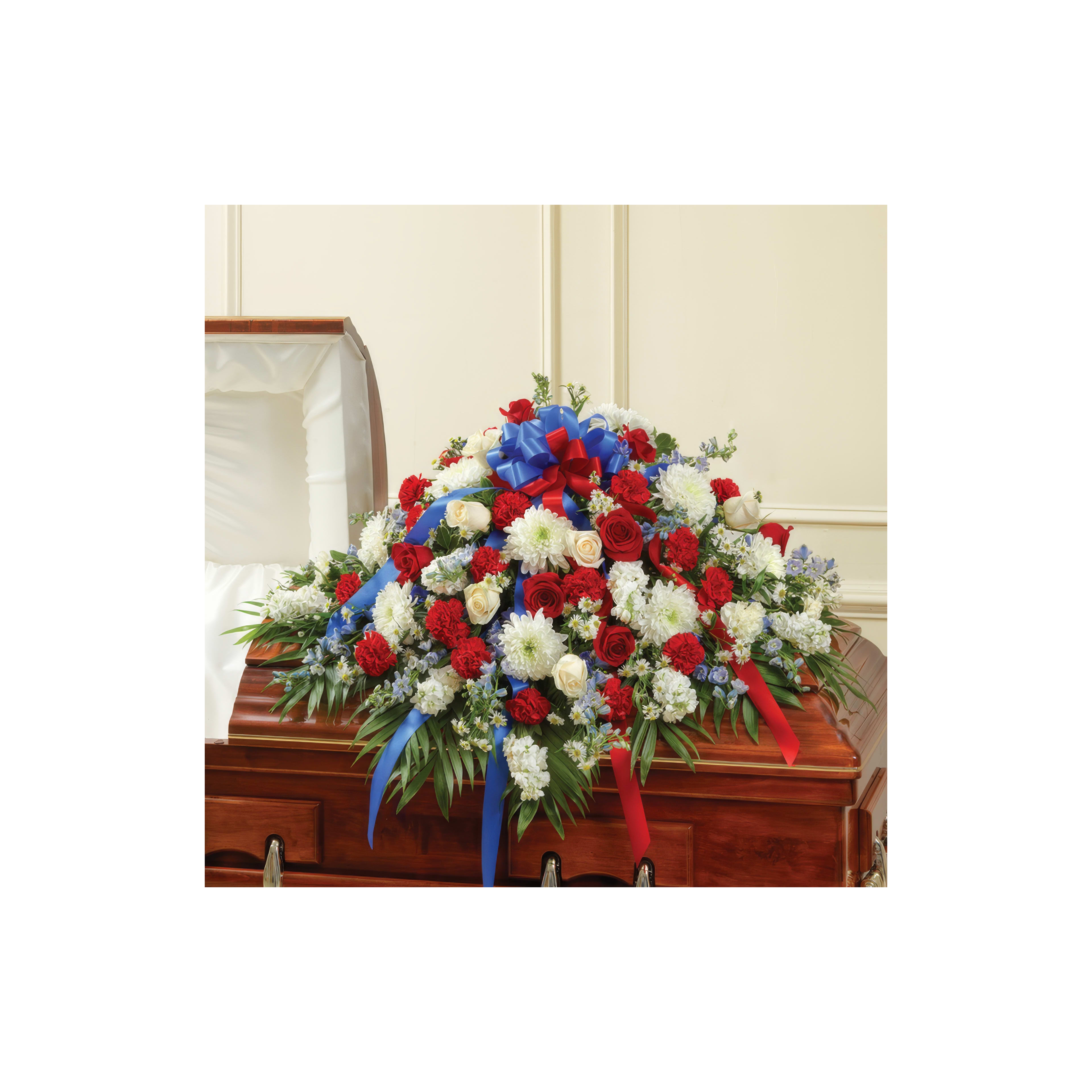 A floral arrangement of red, white, and blue flowers decorates a wooden casket at a memorial.