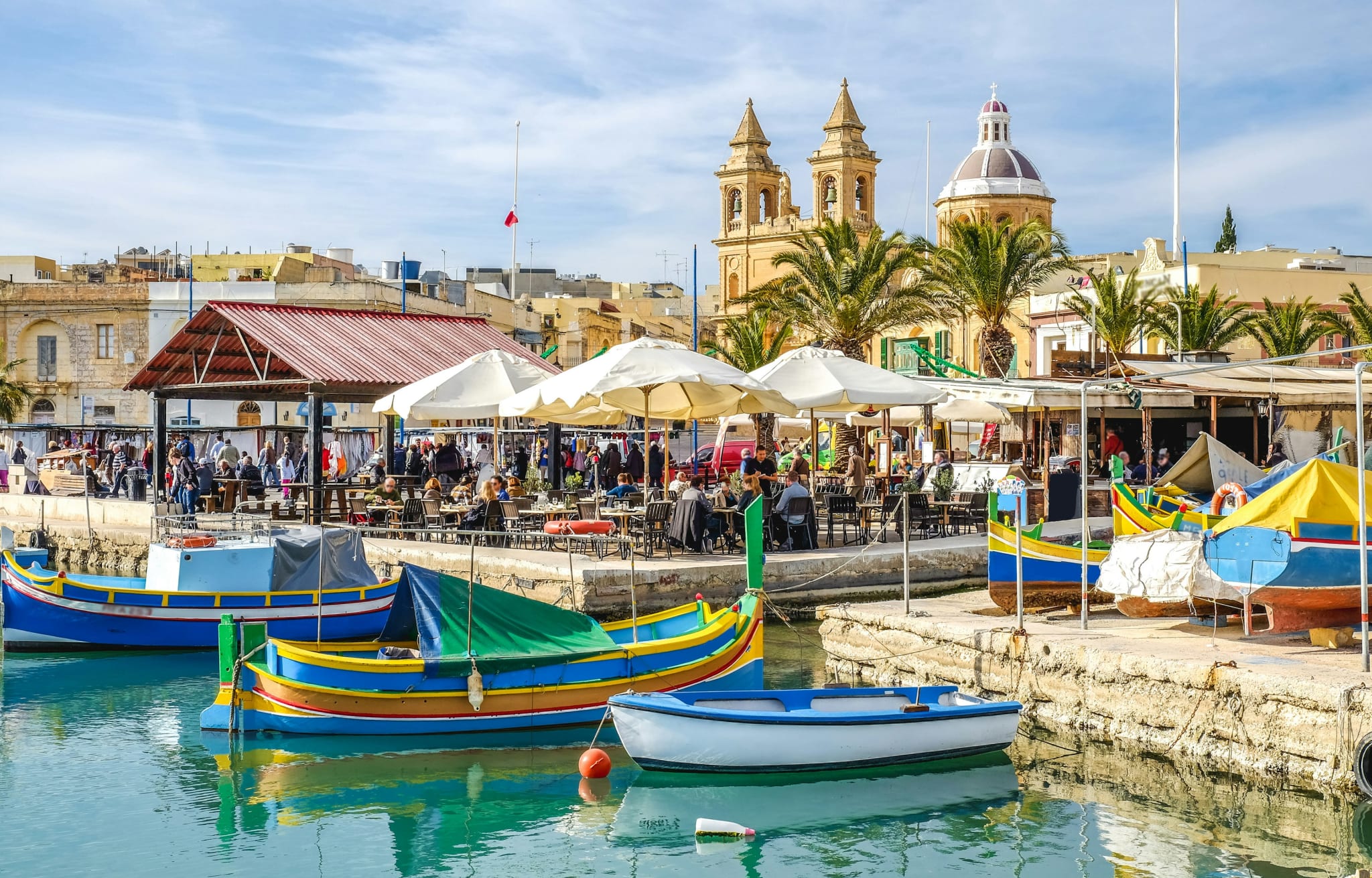 Colourful luzzu fishing boats in a Maltese harbour with a church behind