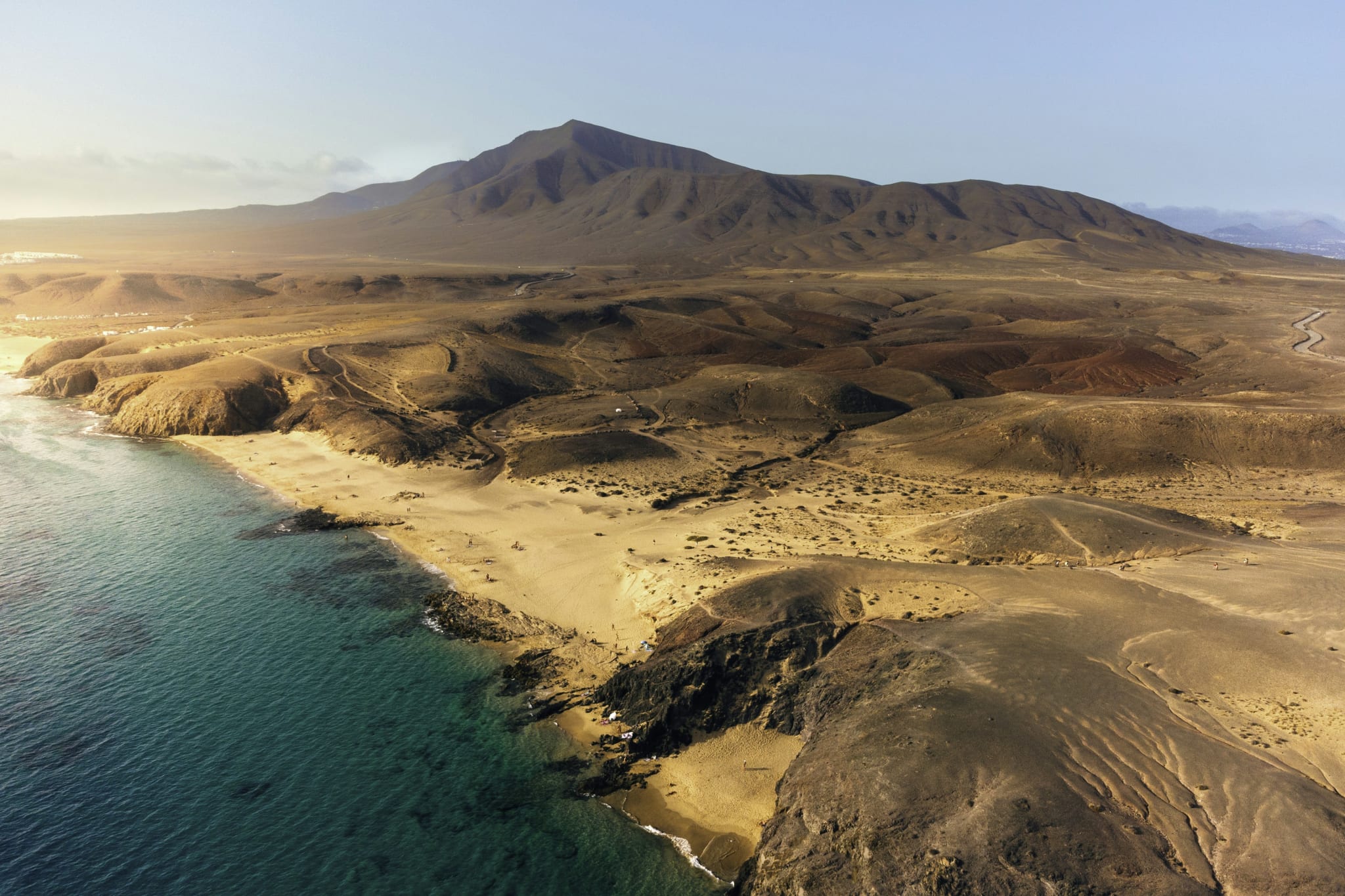 Sandstrand og turkist hav under brune fjell på Kanariøyene sett ovenfra