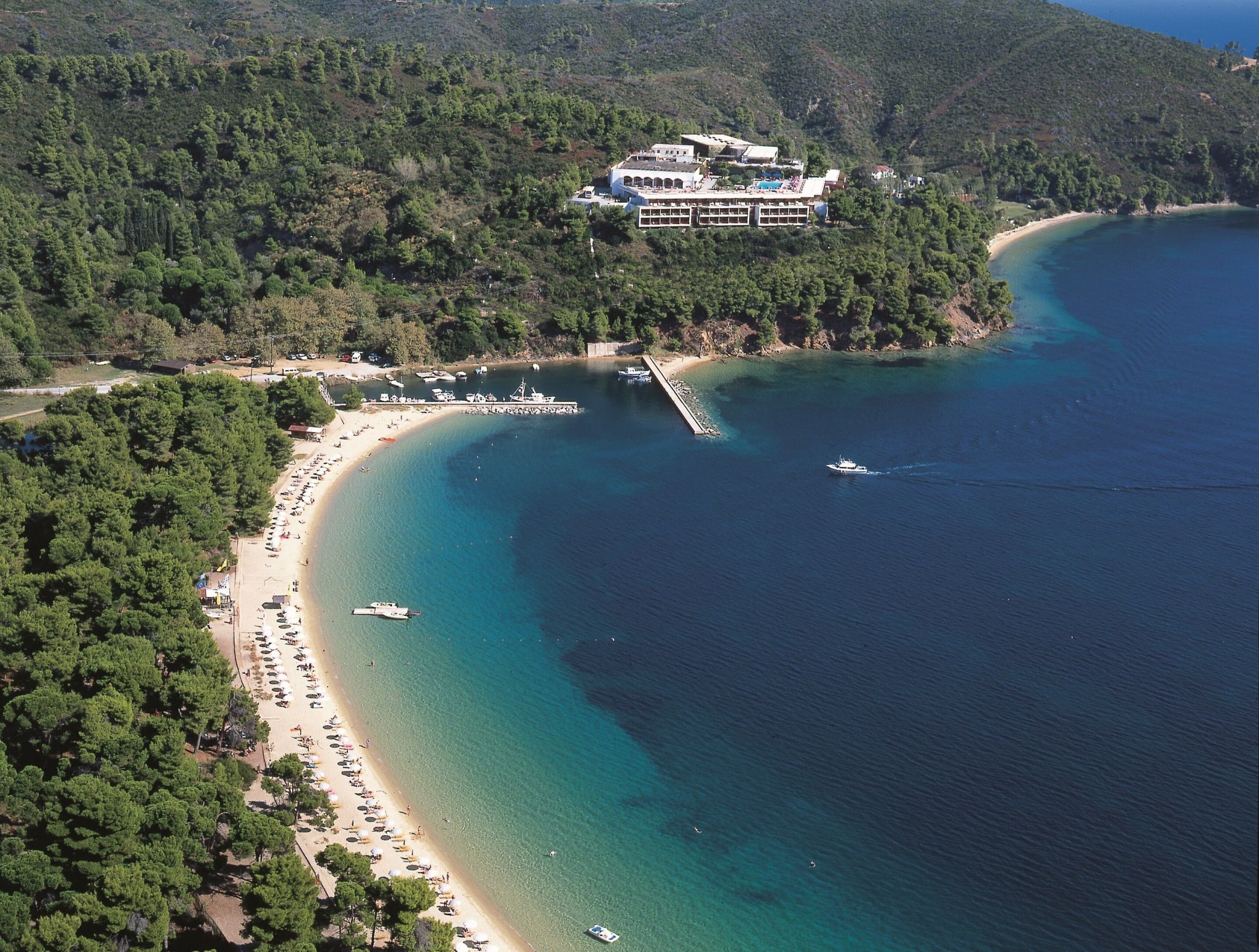 Flyfoto av en sandstrand omgitt av furuskog ved Skiathos Palace på Skiathos