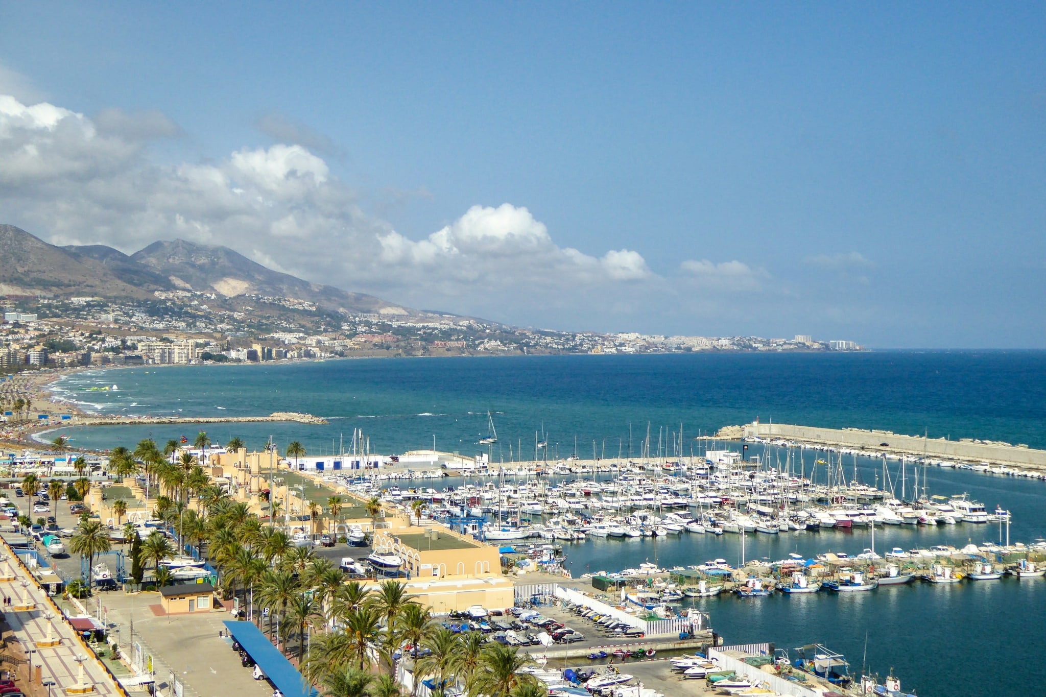 The marina in Fuengirola seen from above, with palm trees, sailing boats and the coast towards Benalmádena