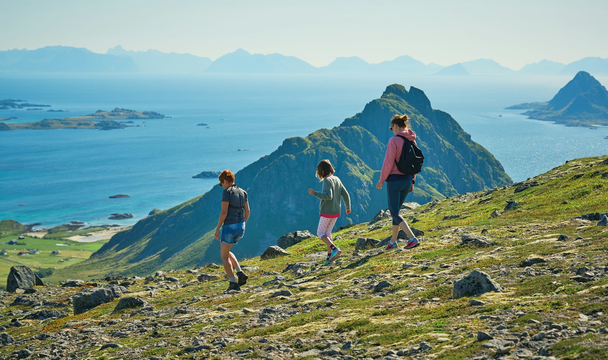 Three hikers on a green mountain ridge above the sea in Bø in Vesterålen