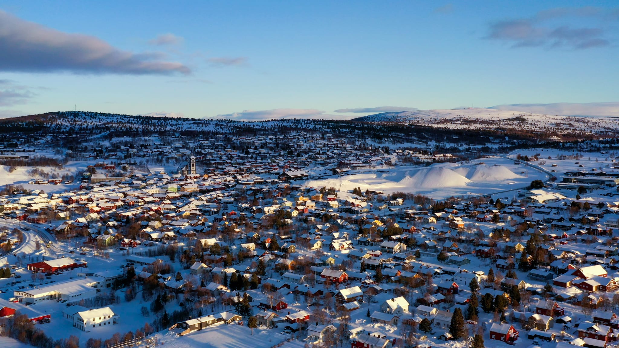 Røros sett ovenfra en vintermorgen, med tømmerhus, snø og fjell i bakgrunnen