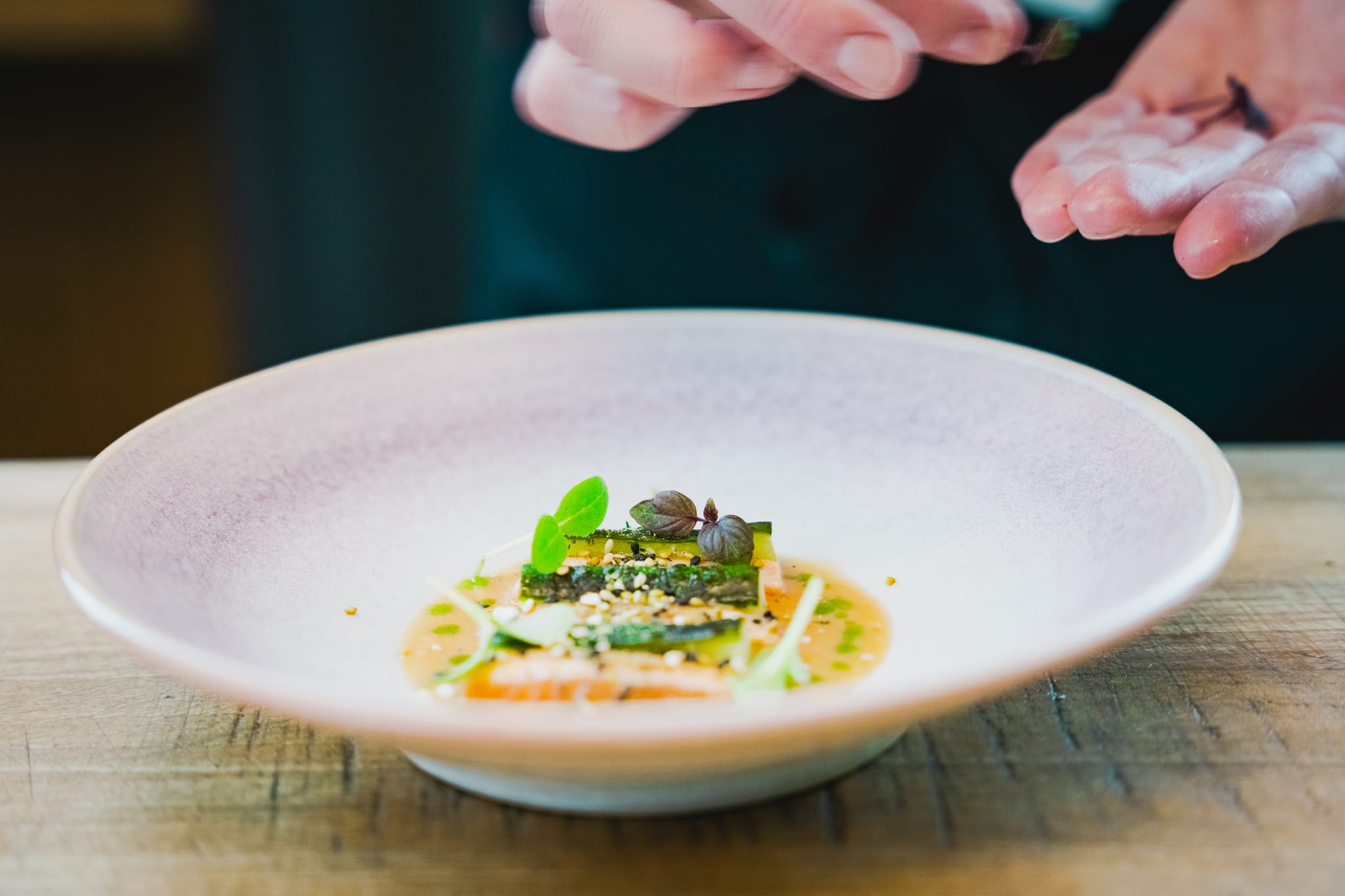 A plated fish dish with green leaves in a white, deep bowl