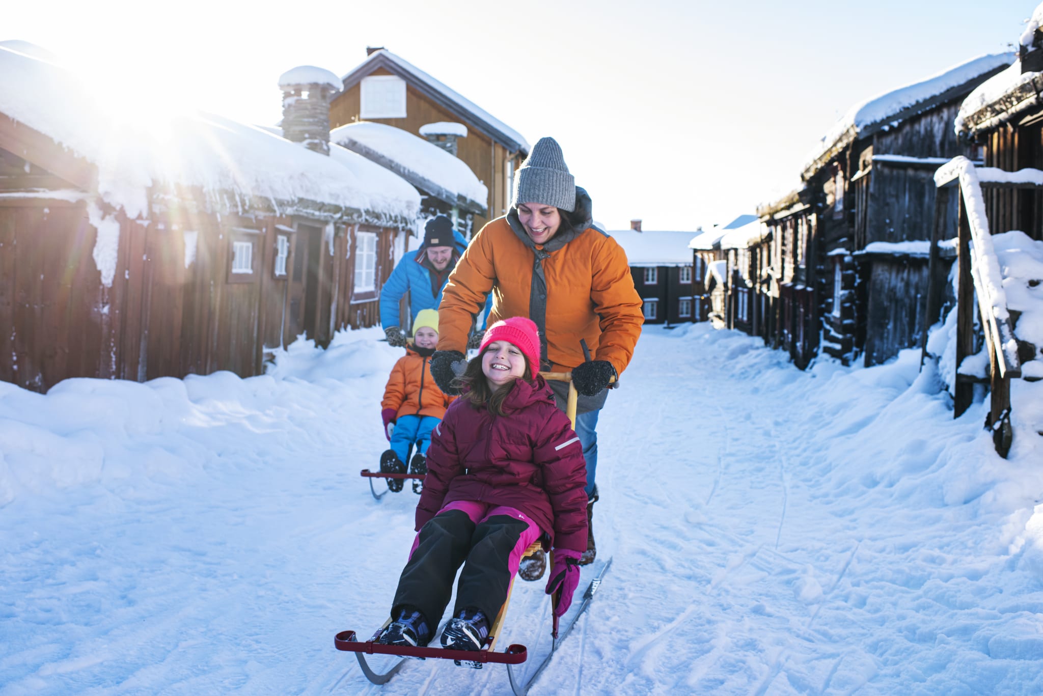 A family on a kick sled in a narrow winter lane between historic timber houses in Røros
