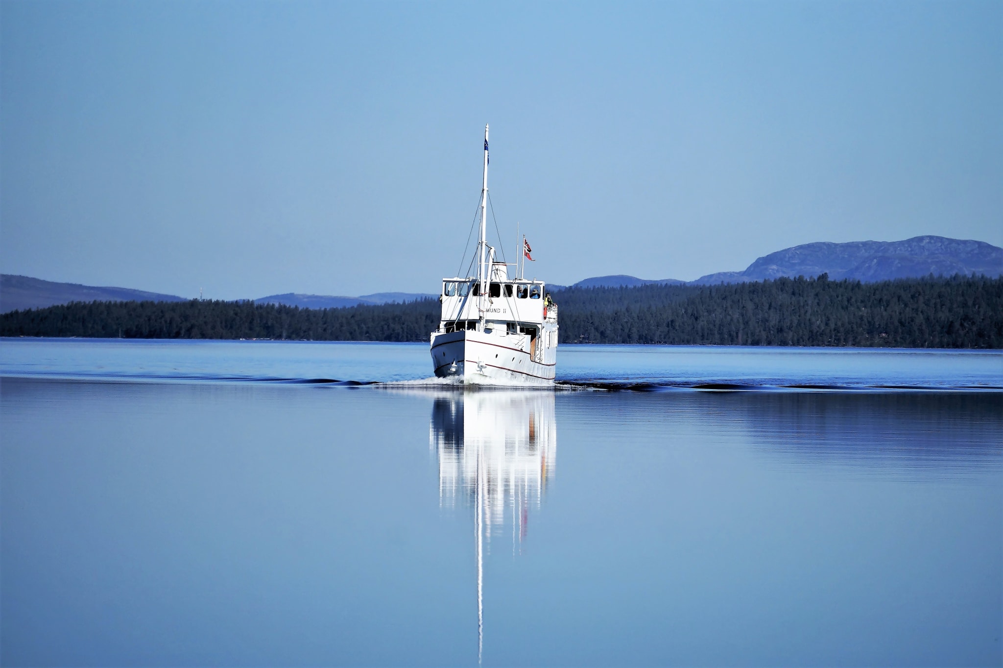 MS Fæmund II sailing on the mirror-calm Lake Femunden with mountains and forest behind
