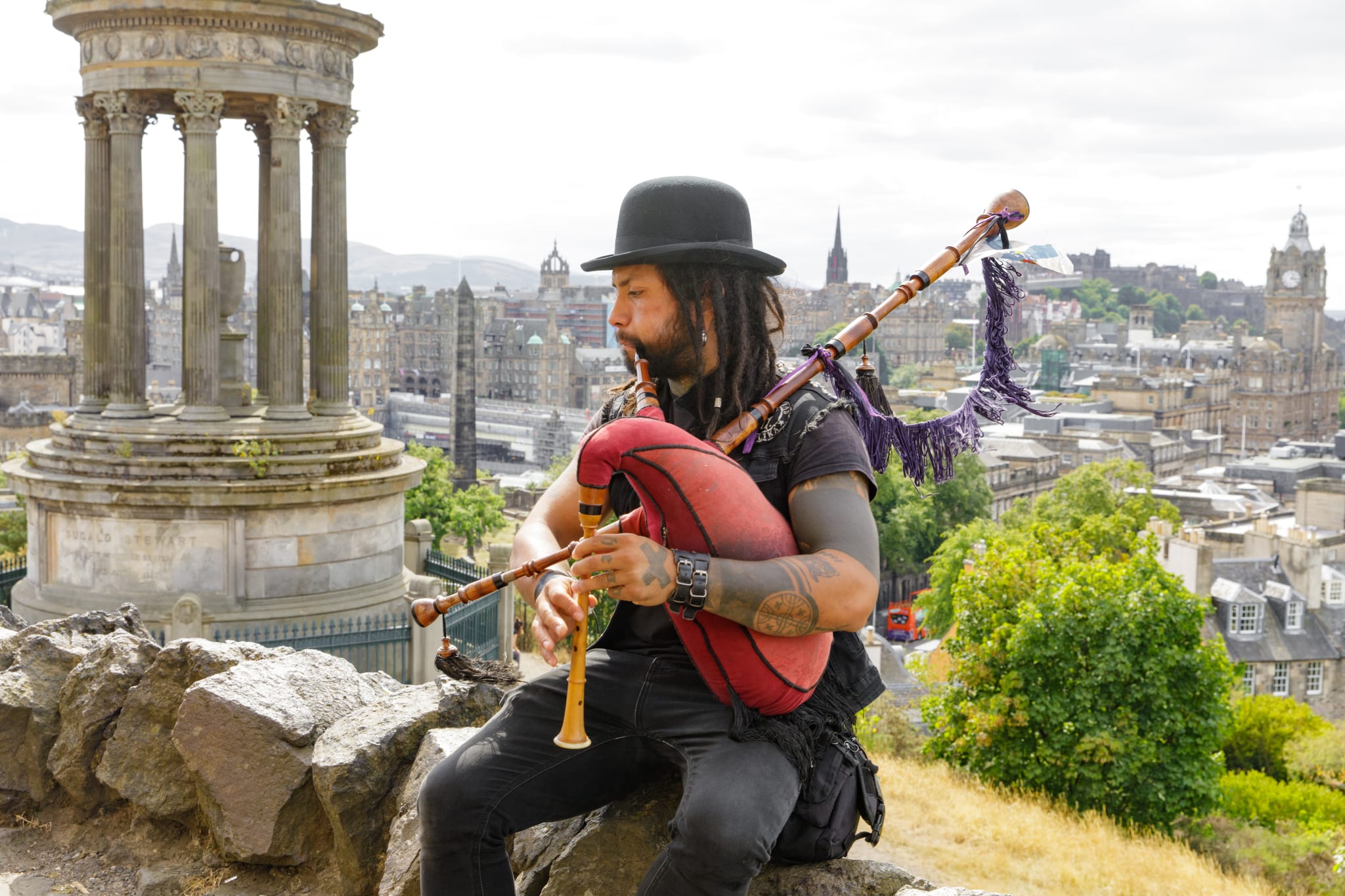 A man in a bowler hat playing the bagpipes on Calton Hill in Edinburgh