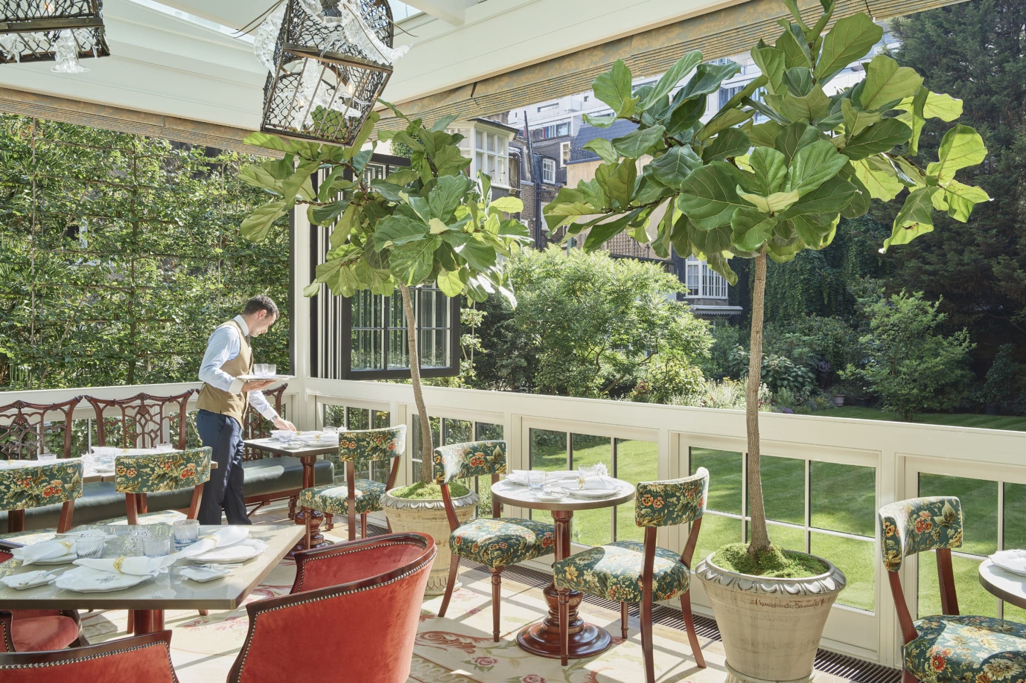 Glass veranda with plants and tables facing the garden at The Goring in London