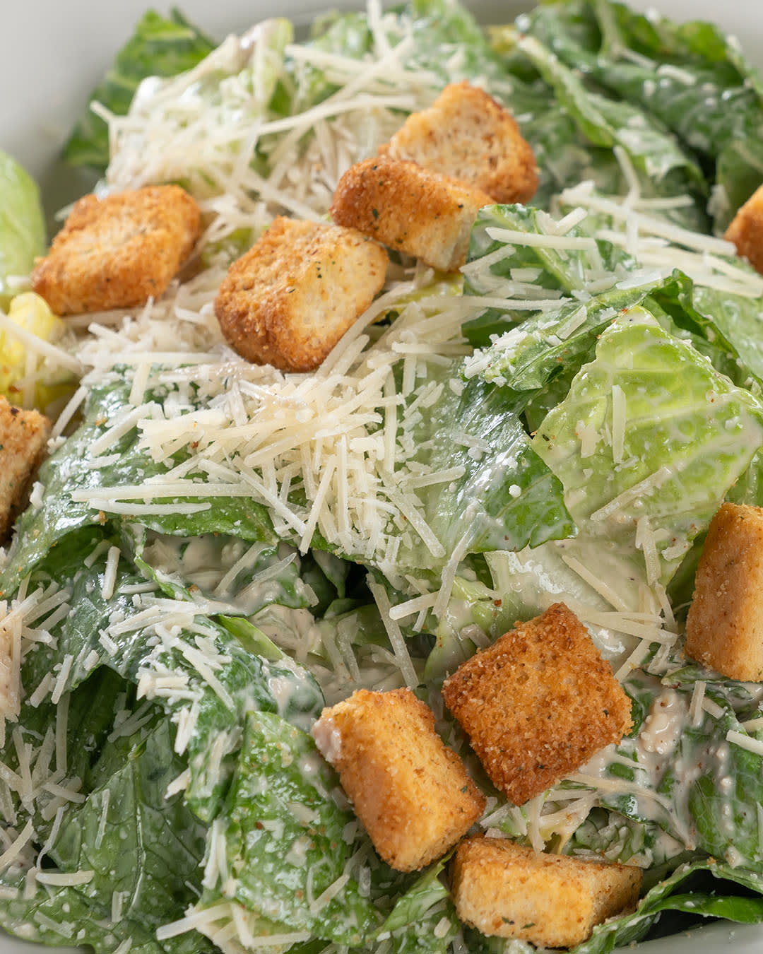 A plate of Caesar salad topped with crunchy croutons and grated Parmesan cheese on a bed of fresh romaine lettuce.