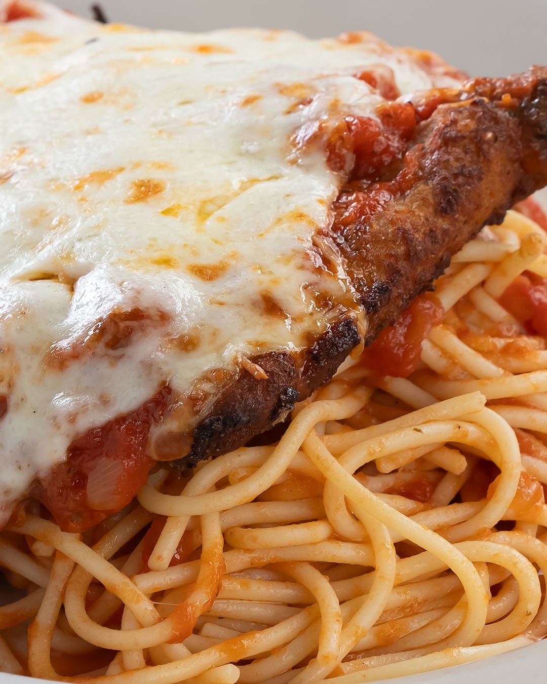 A plate of spaghetti topped with marinara sauce, a breaded chicken cutlet, and melted mozzarella cheese on a white dish.