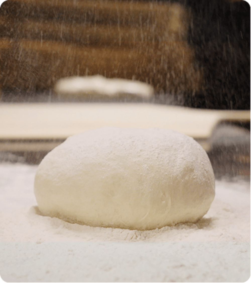 Ball of pizza dough being sprinkled with flour