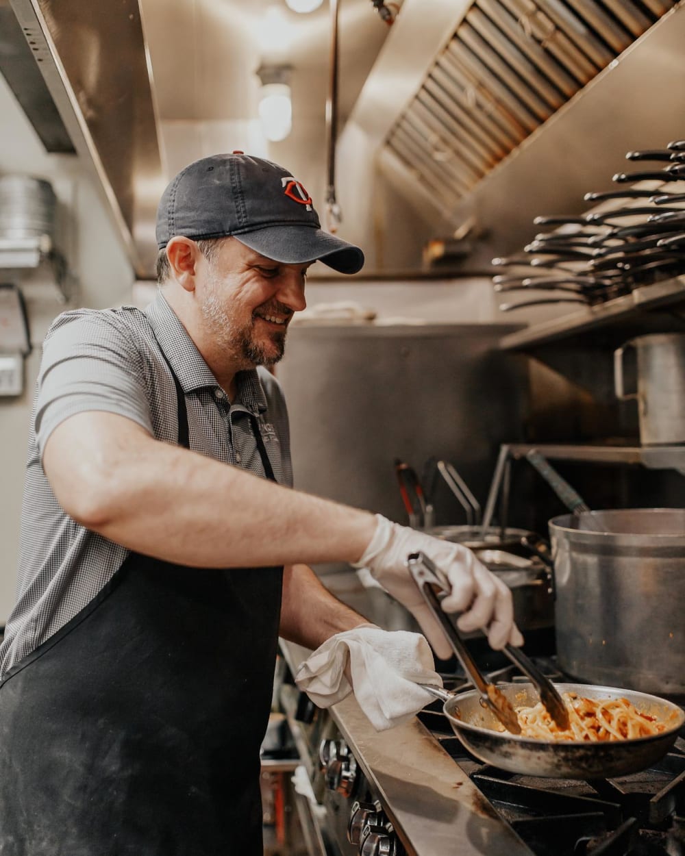Chef in the kitchen mixing pasta with tongs in a stainless pan