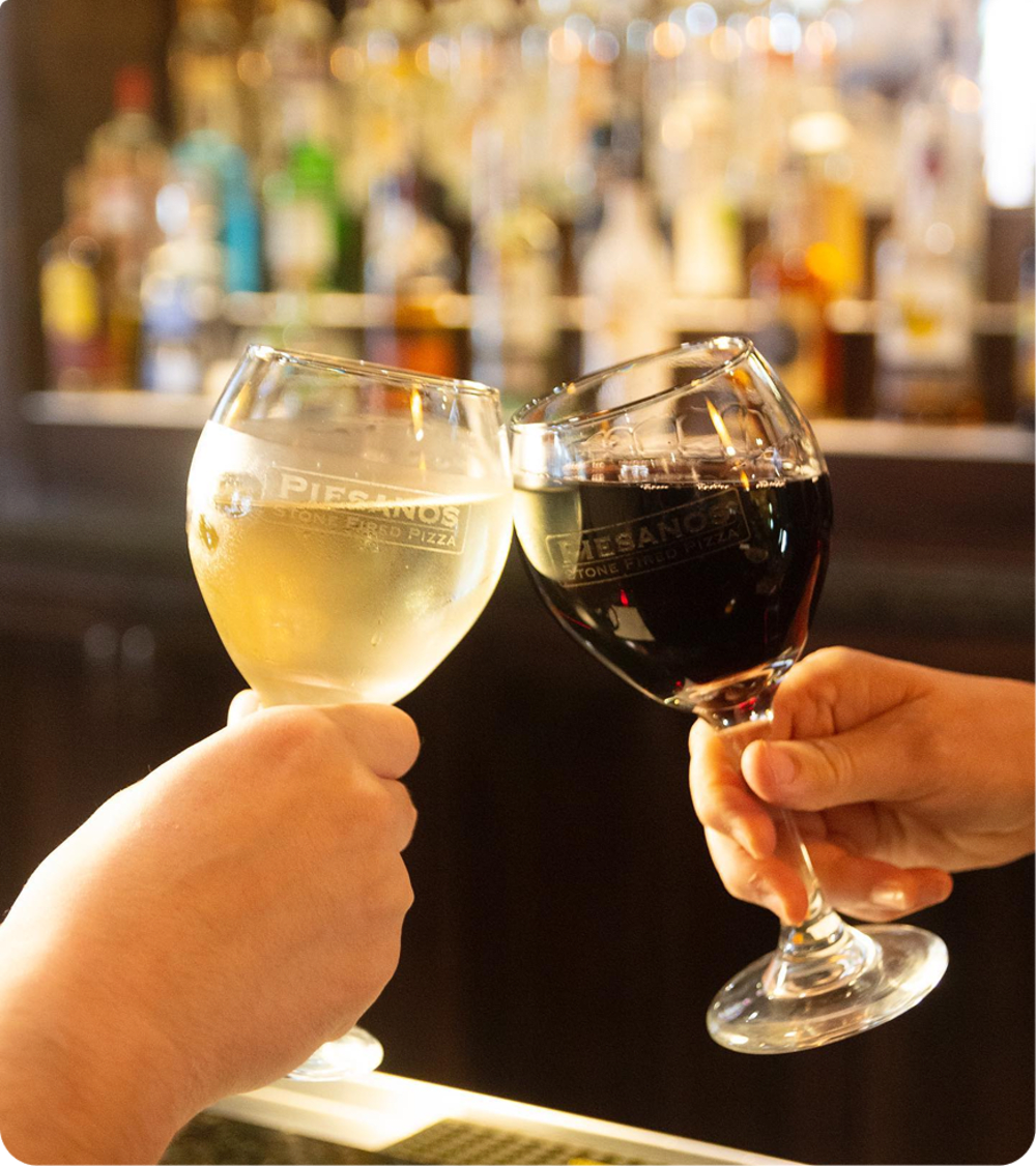 Two hands holding wine glasses in front of the bar