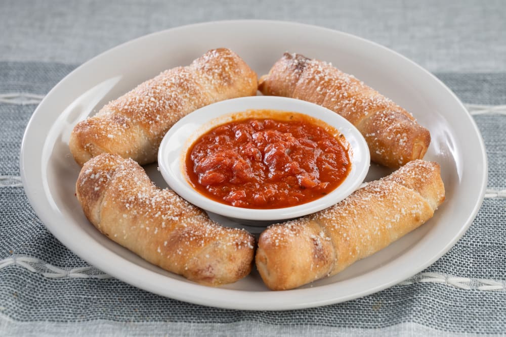 Four pepperoni rolls with bowl of marinara sauce on a white plate