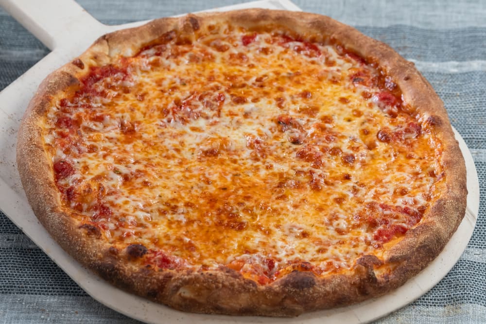 Cheese pizza on a pizza peel on a blue tablecloth