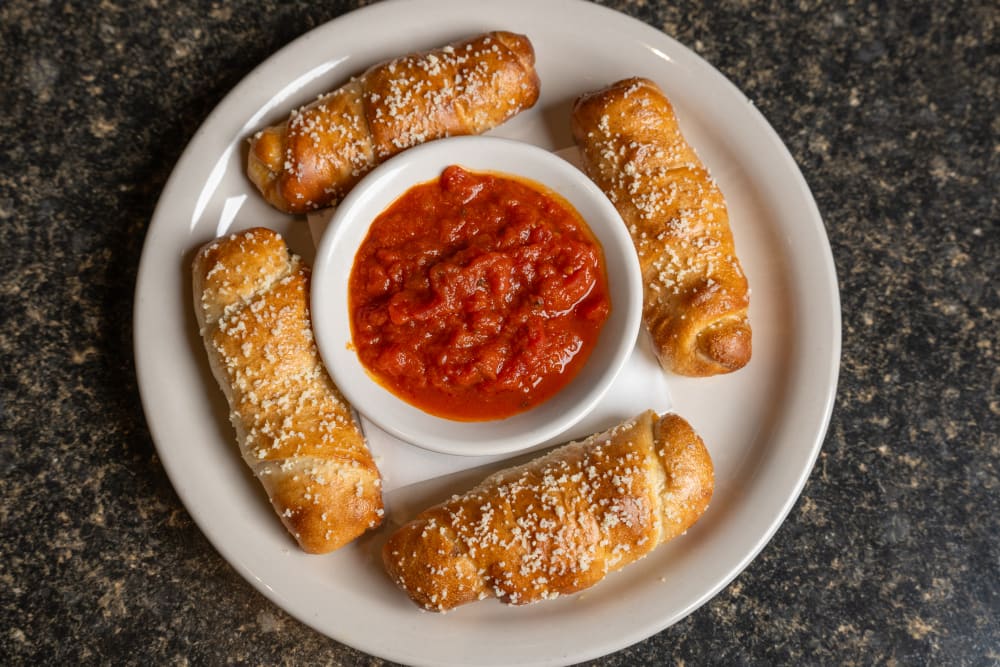 Four pepperoni rolls with bowl of marinara sauce on a white plate