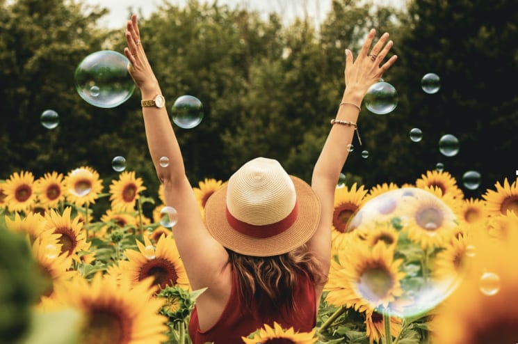 Handen in de lucht in een veld met zonnebloemen en zeepbellen