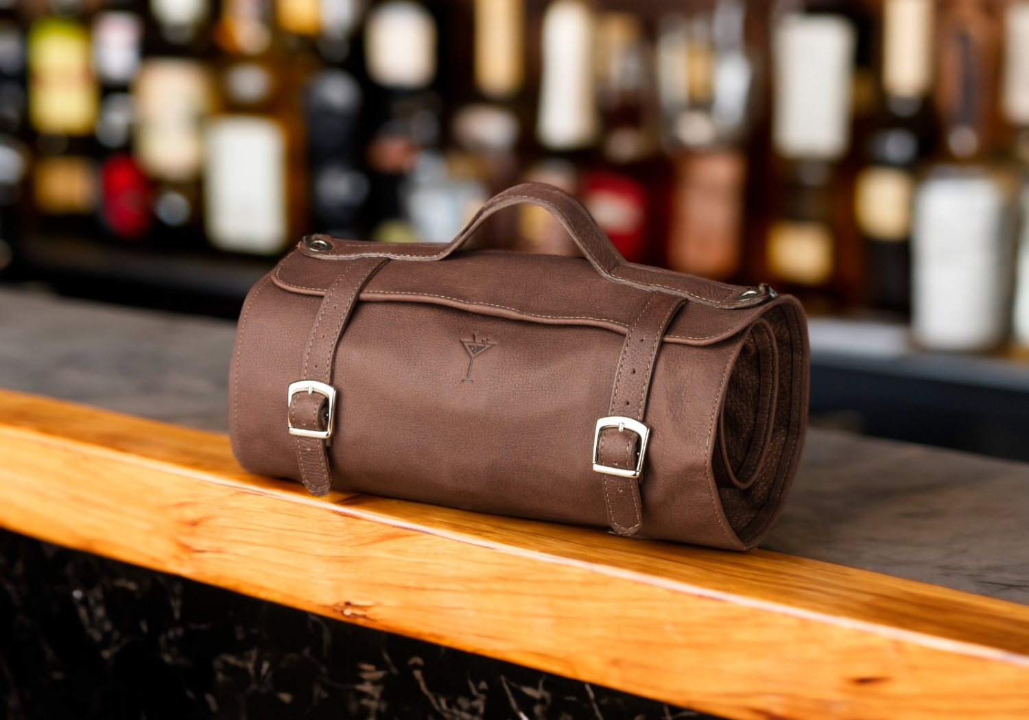 Brown leather duffel bag displayed on a wooden bar counter.