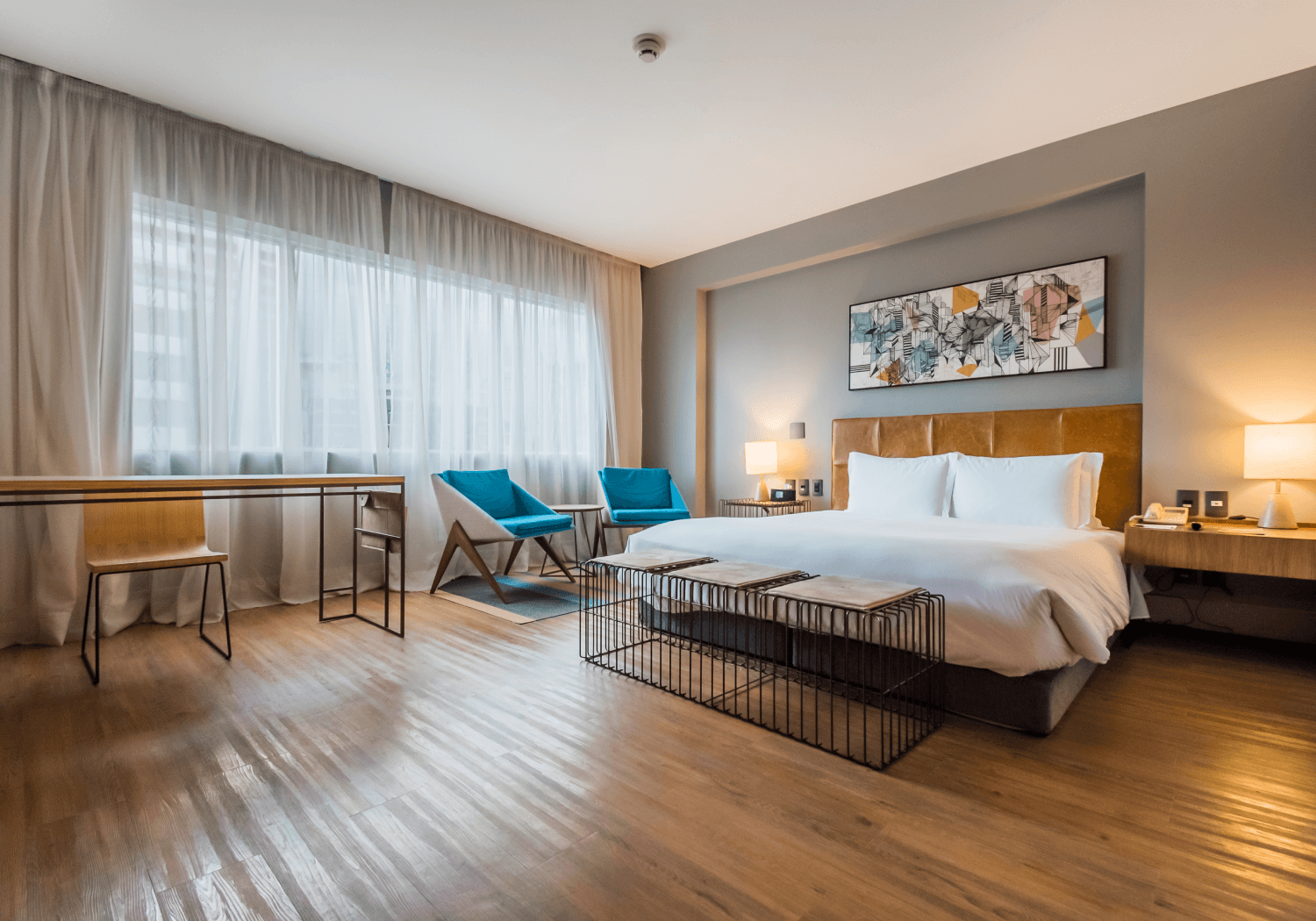 Spacious hotel room with a king-sized bed, wooden flooring, and modern decor.